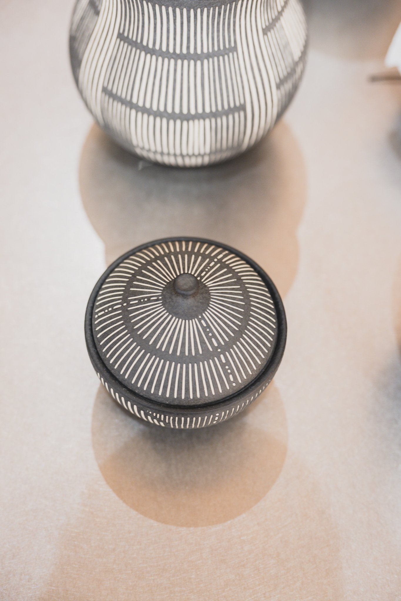 Detail of a charcoal ceramic piece with a radiating line pattern, one of many small-batch pieces on the shelves