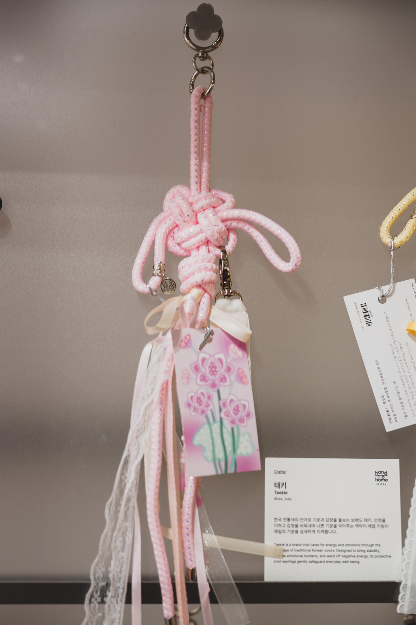 A pink norigae-style knot keyring from the brand Taekie, with its bilingual maker card