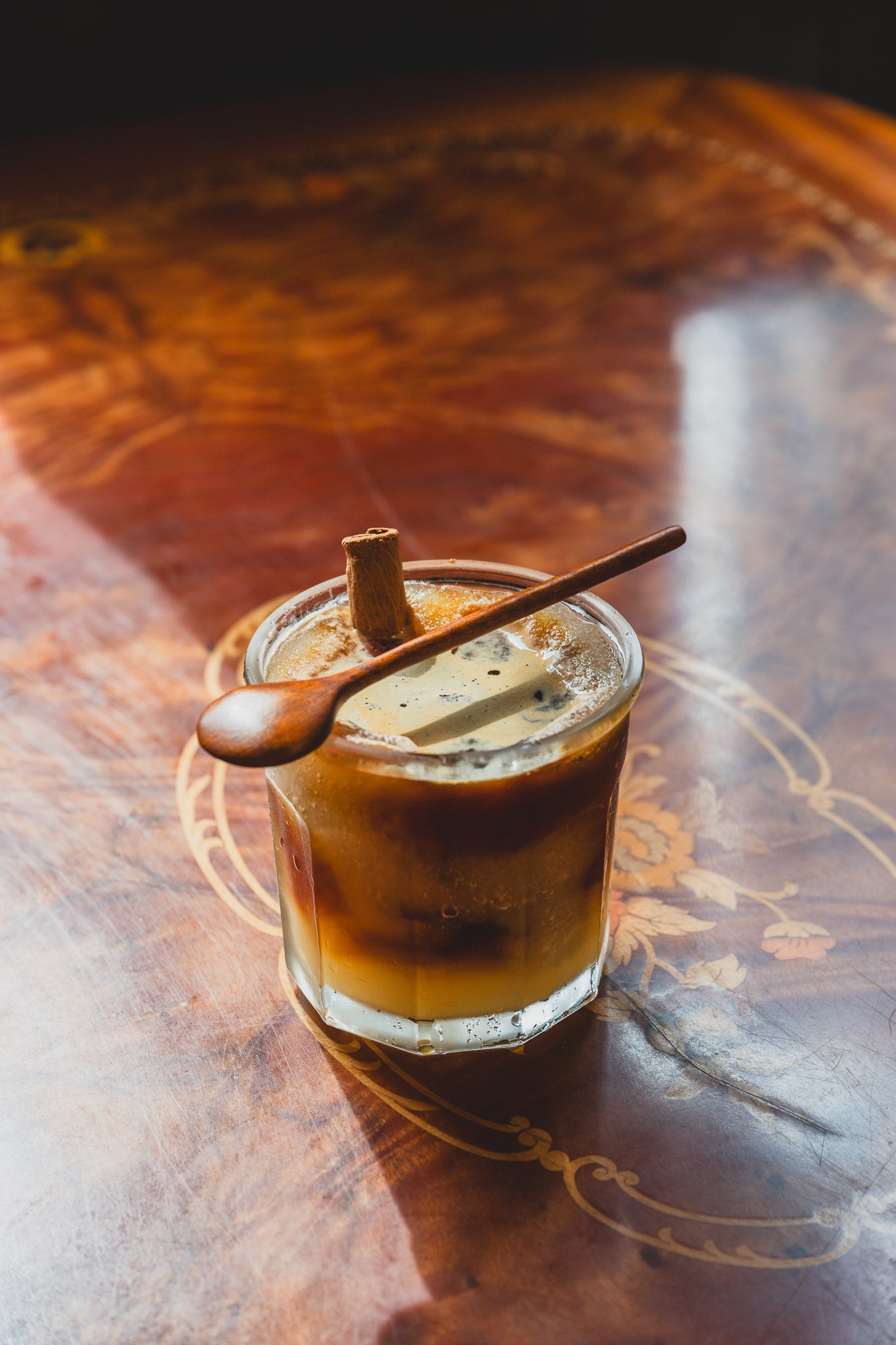 Close-up of the Sujeonggwa-in-gabe drink, showing the layered dark punch and espresso with a cinnamon stick standing in the glass