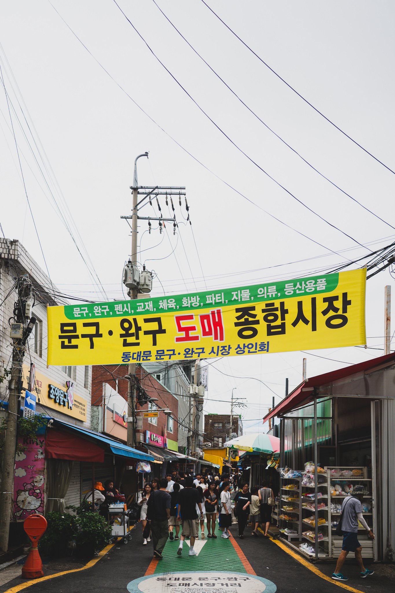 A yellow banner reading "Wholesale Stationery and Toy Market" hangs over the alley entrance