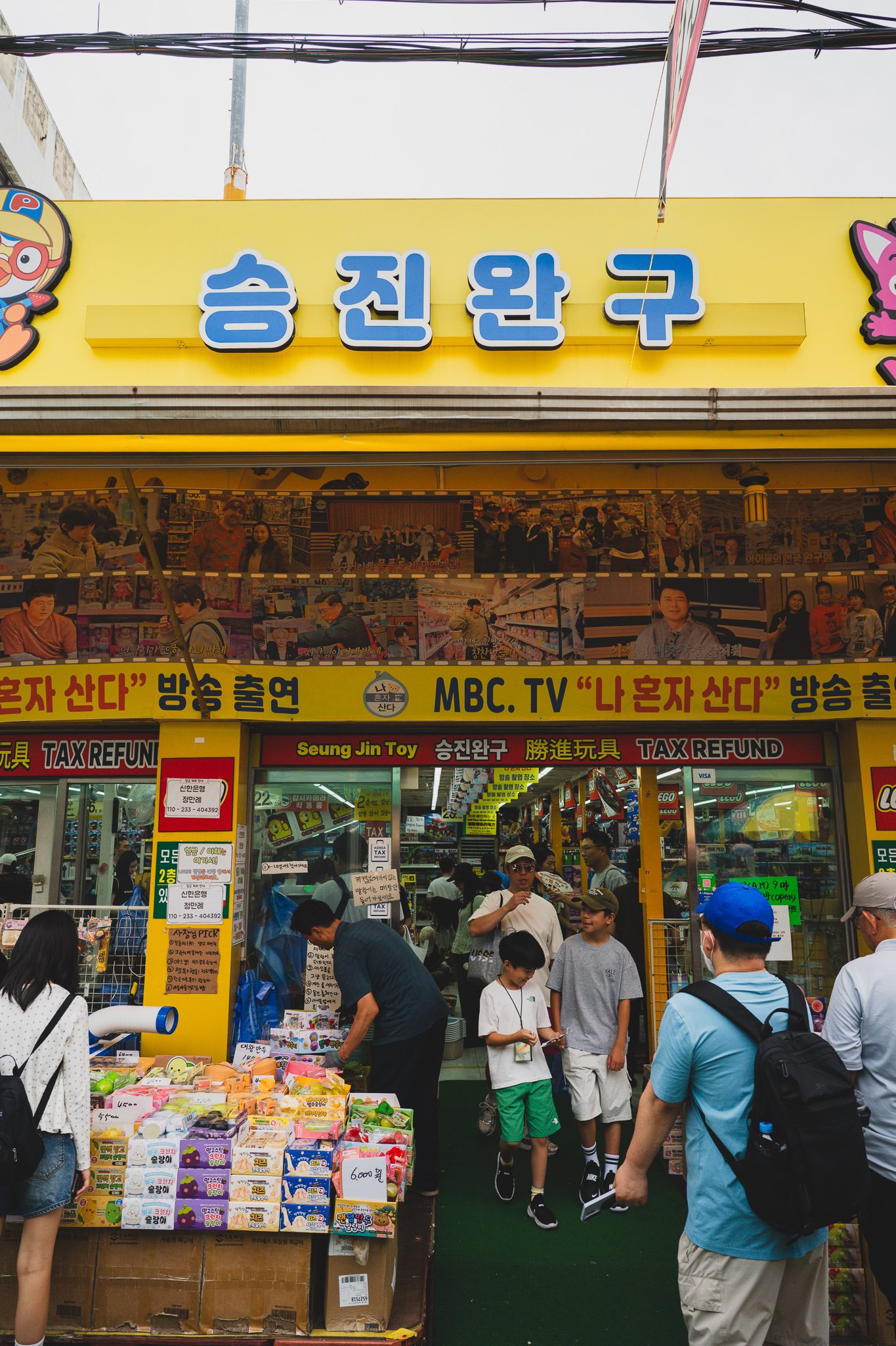 Yellow "Seung Jin Toy" signage with a strip of photos noting an appearance on MBC's "I Live Alone"