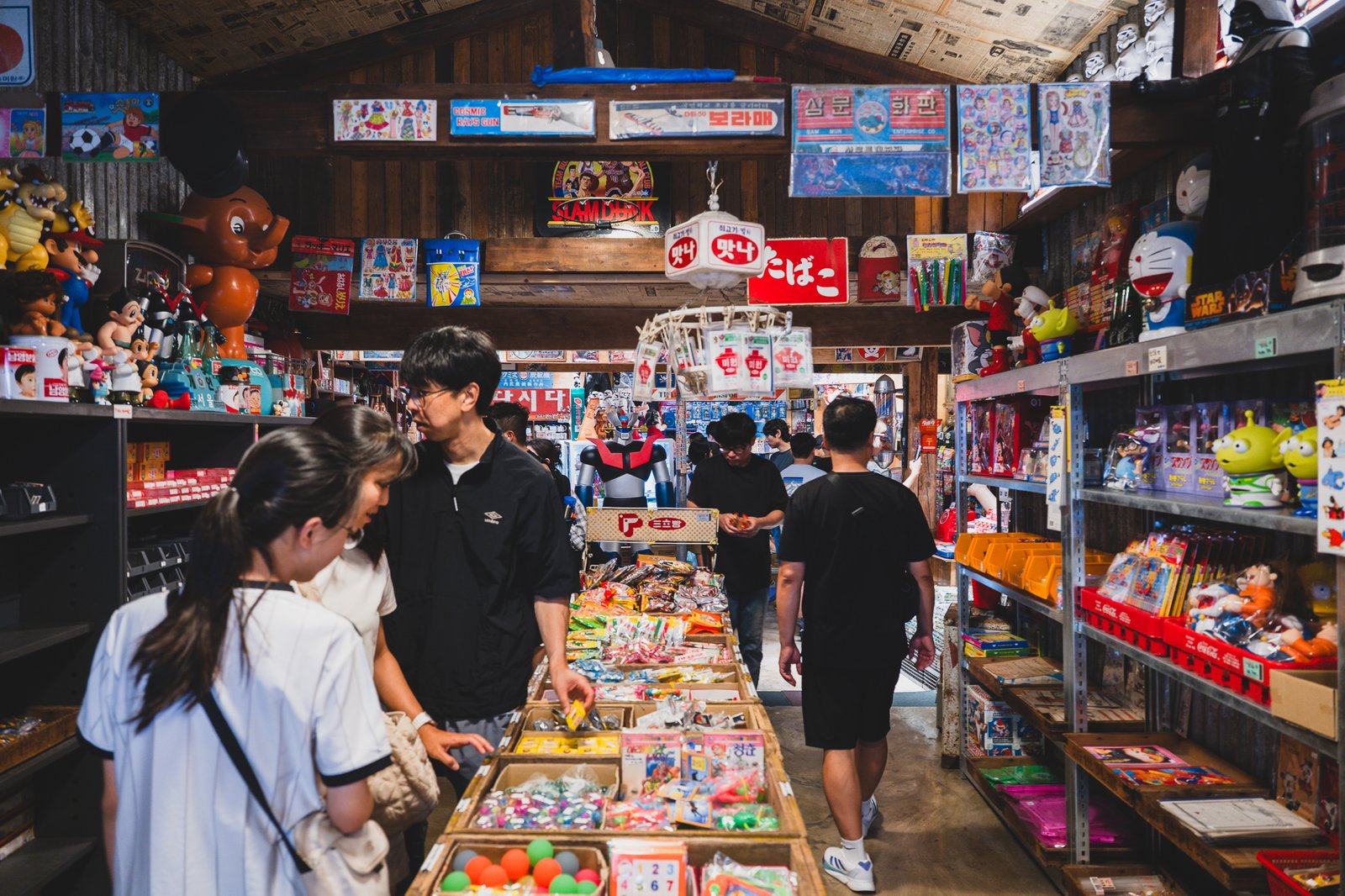 Inside a shop with a ceiling papered in old newspaper, Doraemon and Star Wars figures displayed alongside old-fashioned penny candy
