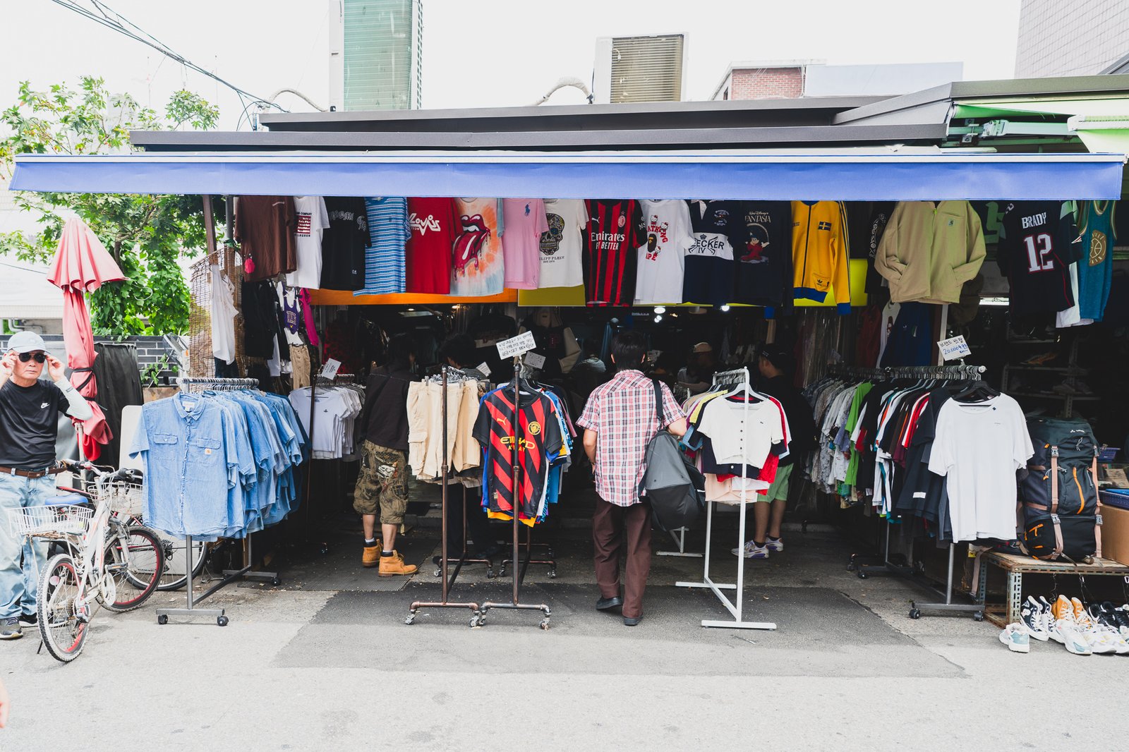 A packed Dongmyo clothing stall with soccer and NFL jerseys, band and Disney graphic tees, and other vintage pieces hanging side by side