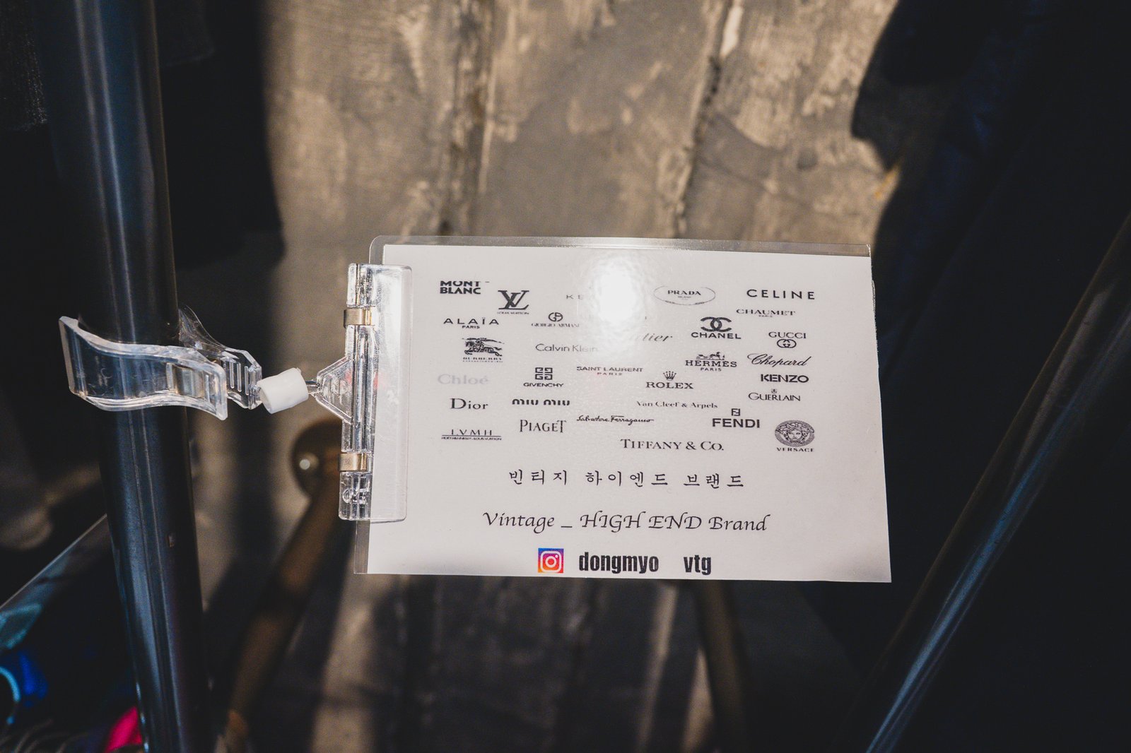 A hand-lettered sign at a Dongmyo stall reading Vintage HIGH END Brand, listing Louis Vuitton, Chanel, Prada, Celine, Hermes, Gucci, Rolex, Dior, Miu Miu, Fendi, and Versace