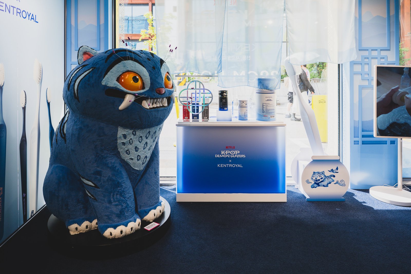 Life-size plush mascot of Derpy, the blue tiger character from KPop Demon Hunters, standing near the store entrance