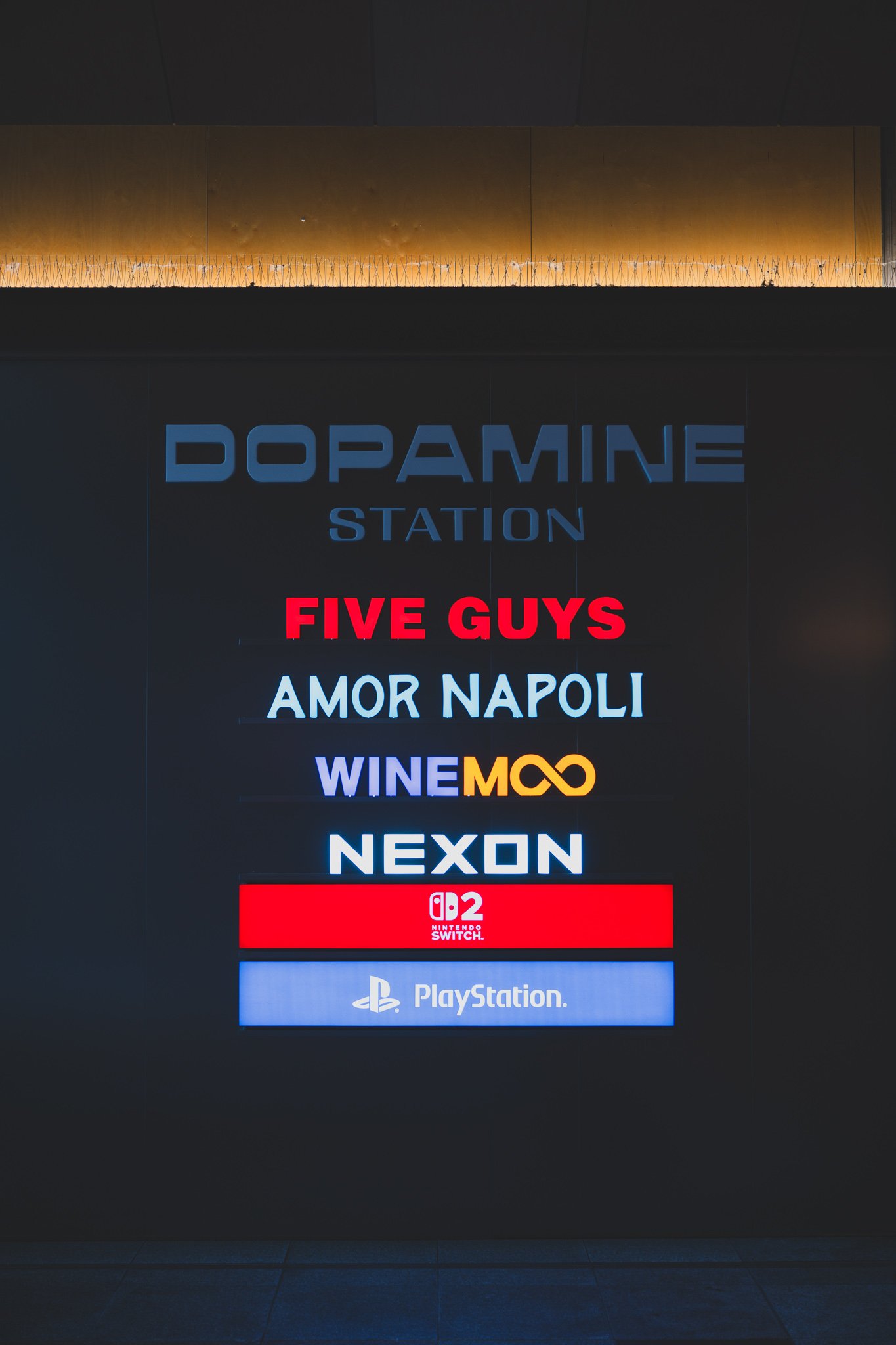 Signage reading "DOPAMINE STATION" with logos for Five Guys, Amor Napoli, Winemoo, Nexon, Nintendo Switch 2, and PlayStation displayed underneath