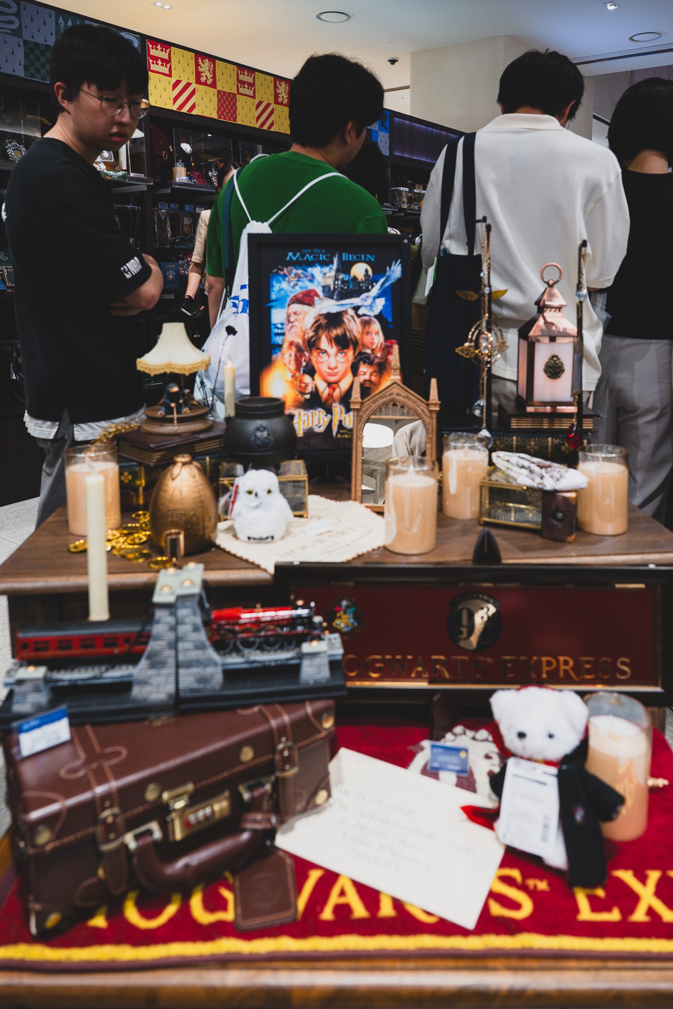 A display table set up like a scene from the films, with a Hogwarts Express miniature model, a Hedwig plush, framed movie posters, a travel trunk, and candle props arranged together