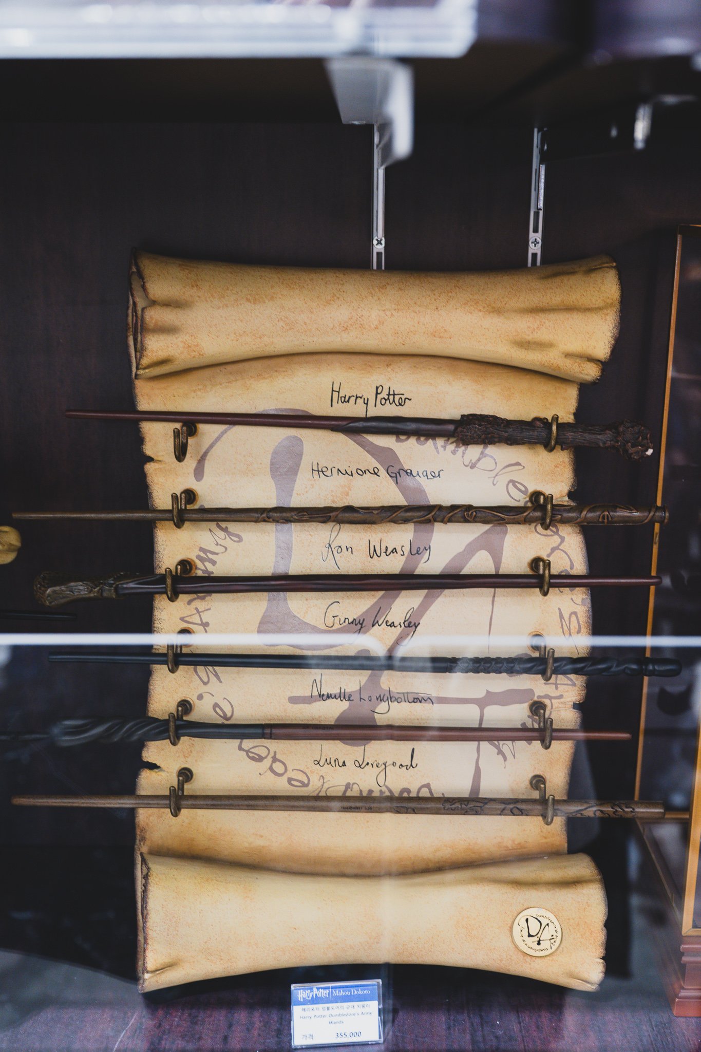 A display of six wands mounted together, representing Harry Potter, Hermione Granger, Ron Weasley, Ginny Weasley, Neville Longbottom, and Luna Lovegood, with a price tag of ₩355,000