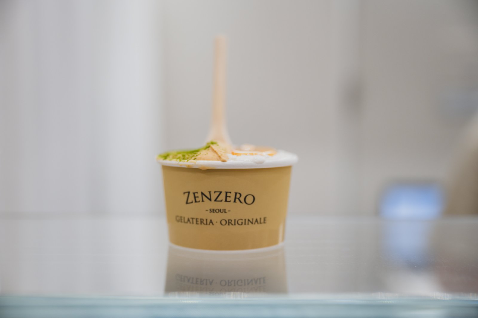 A completed ZENZERO gelato cup, half beige with a green powder dusting, half white with honey drizzled over the top