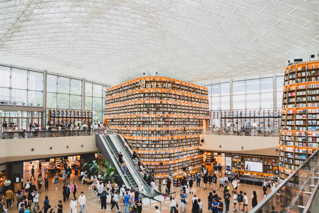 Two towering bookshelves rising about 13 meters at Starfield Library, connected by an escalator, with the Hangul sign "별마당도서관" lit up across the front