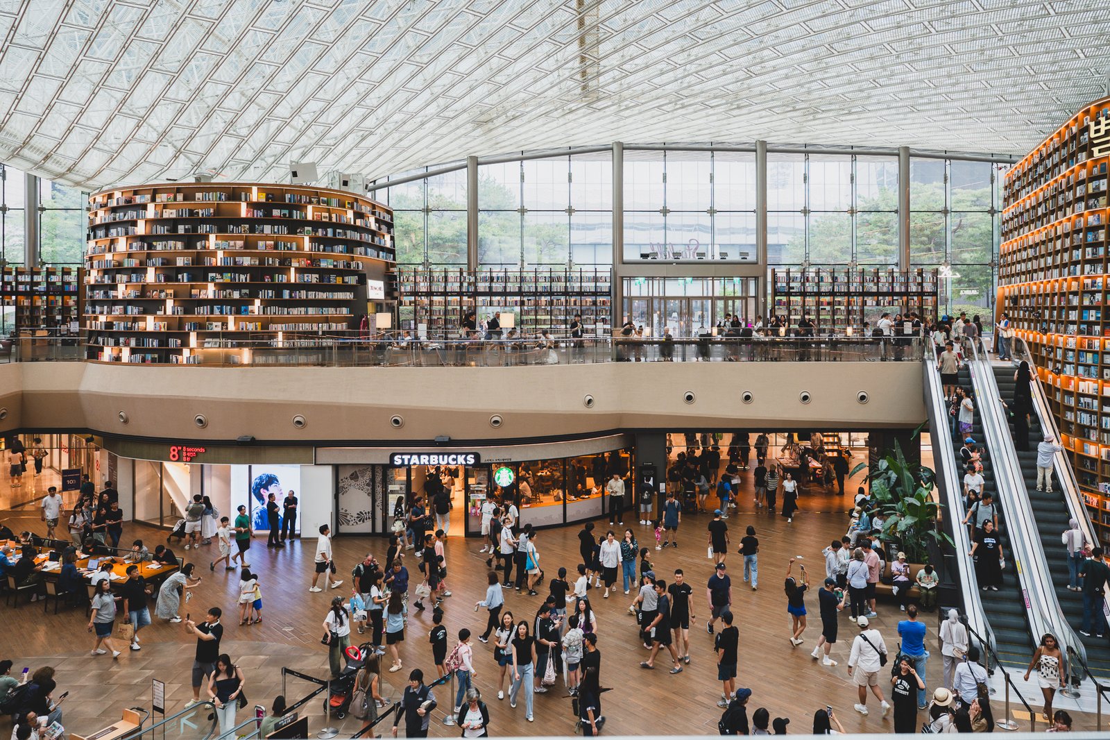 A second angle of the towering bookshelves seen from across the plaza, with the Starfield sign and a Starbucks visible on the level below — showing how the library anchors the entire center of the mall