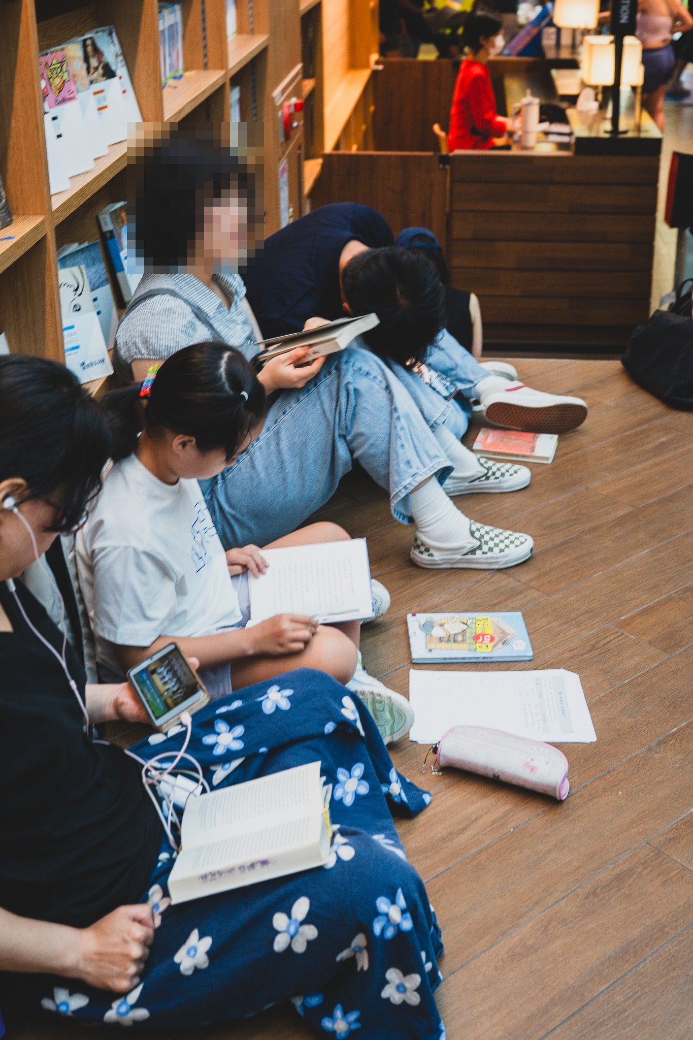 Children sitting on the floor between the bookshelves reading, with books, notebooks, and a pencil case spread out around them