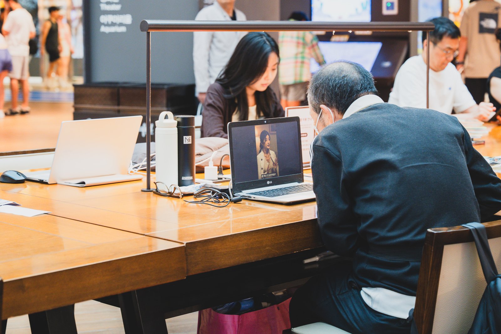 A closer view down the same communal table, with people reading, watching videos, and talking quietly while seated side by side