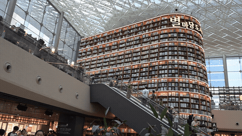 A short walkthrough clip riding the escalator up past the book tower and down into the crowd around the reading tables below — closer to what the space actually feels like in motion than any single photo