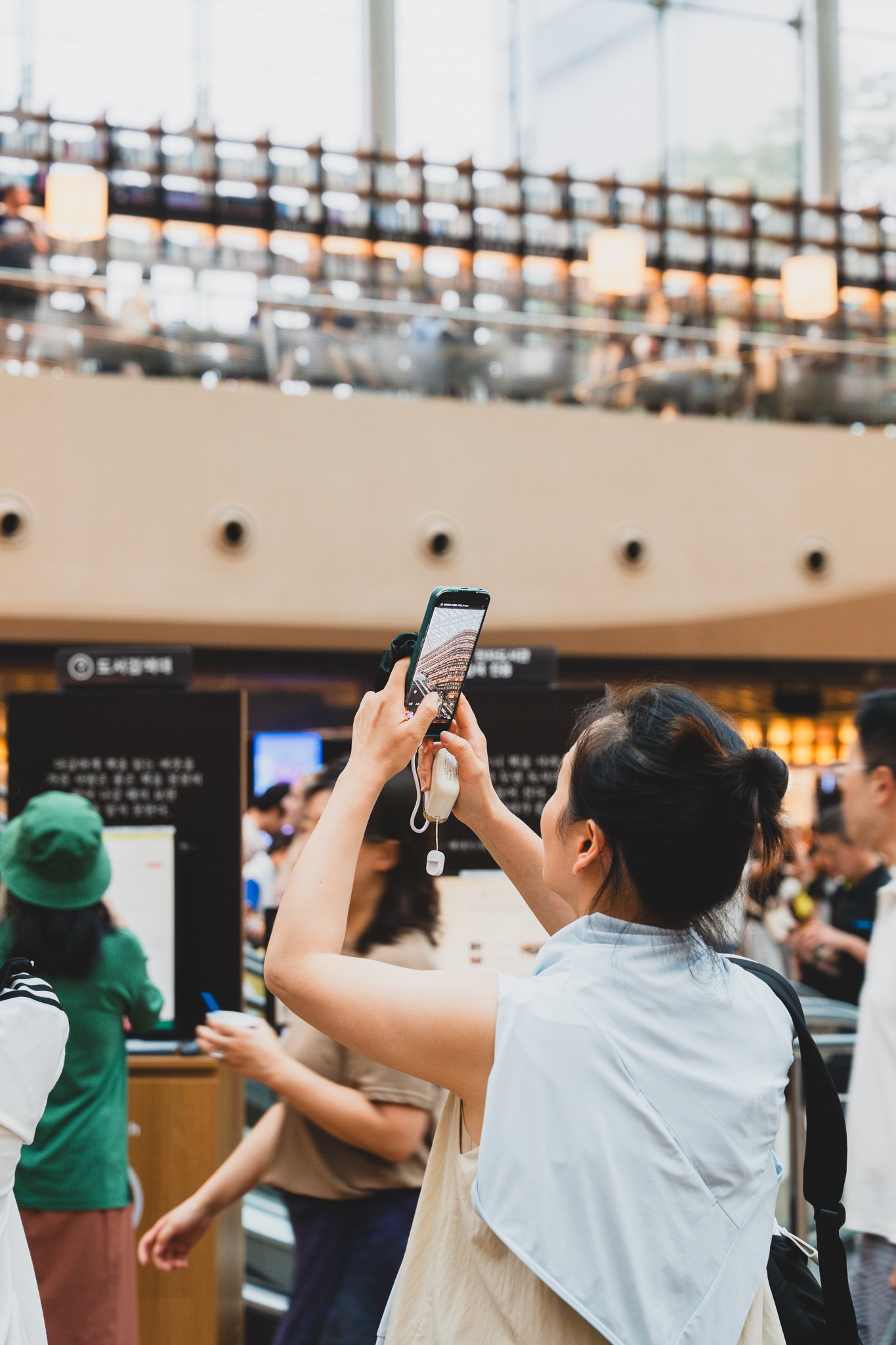 A woman holding up her phone to photograph the bookshelf towers from below, with more visitors doing the same in the background near the information desk
