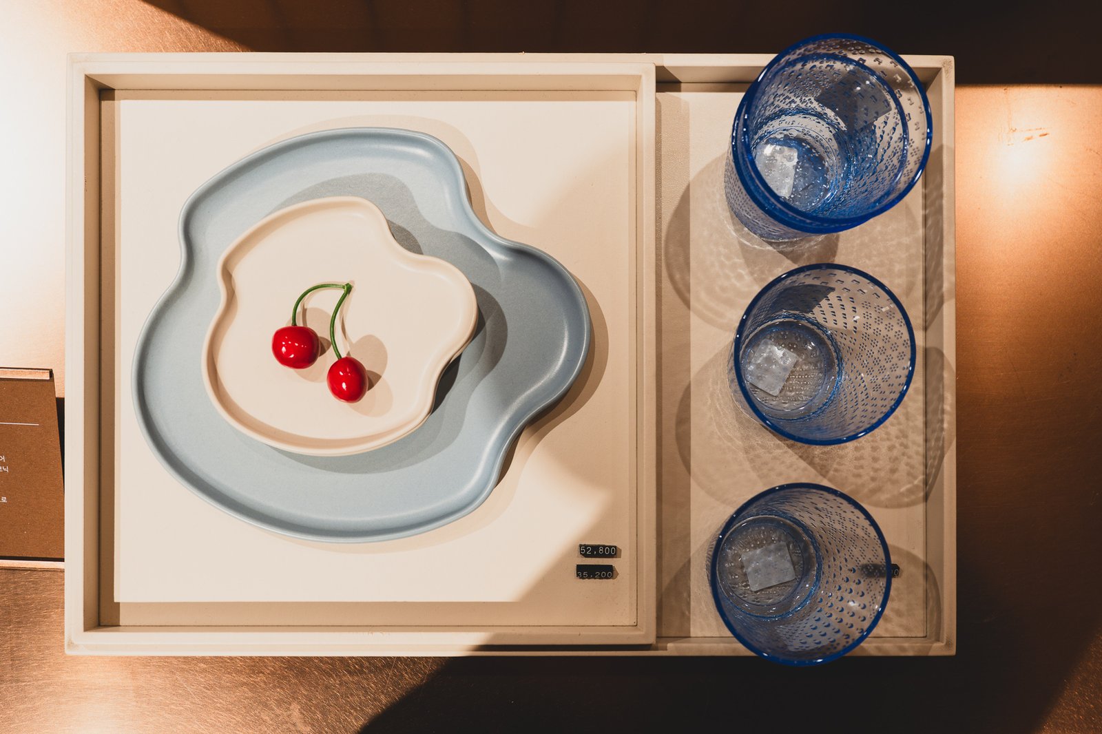 A cloud-shaped ceramic plate set with cherry-shaped objects and textured blue glassware, priced at 52,800 and 35,200 won