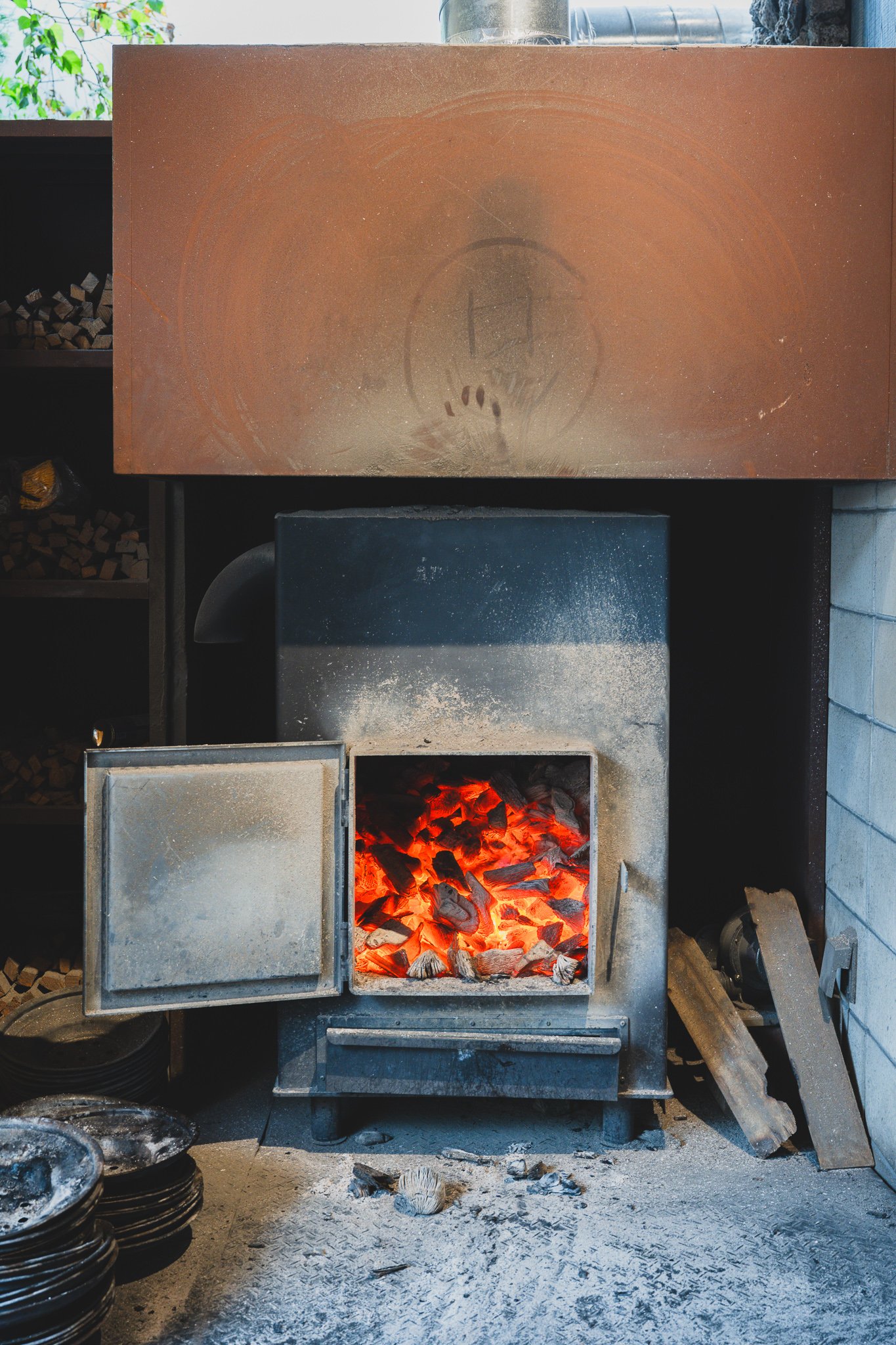 Glowing red charcoal burning inside a traditional furnace at the restaurant, with stacked raw charcoal blocks on shelves nearby