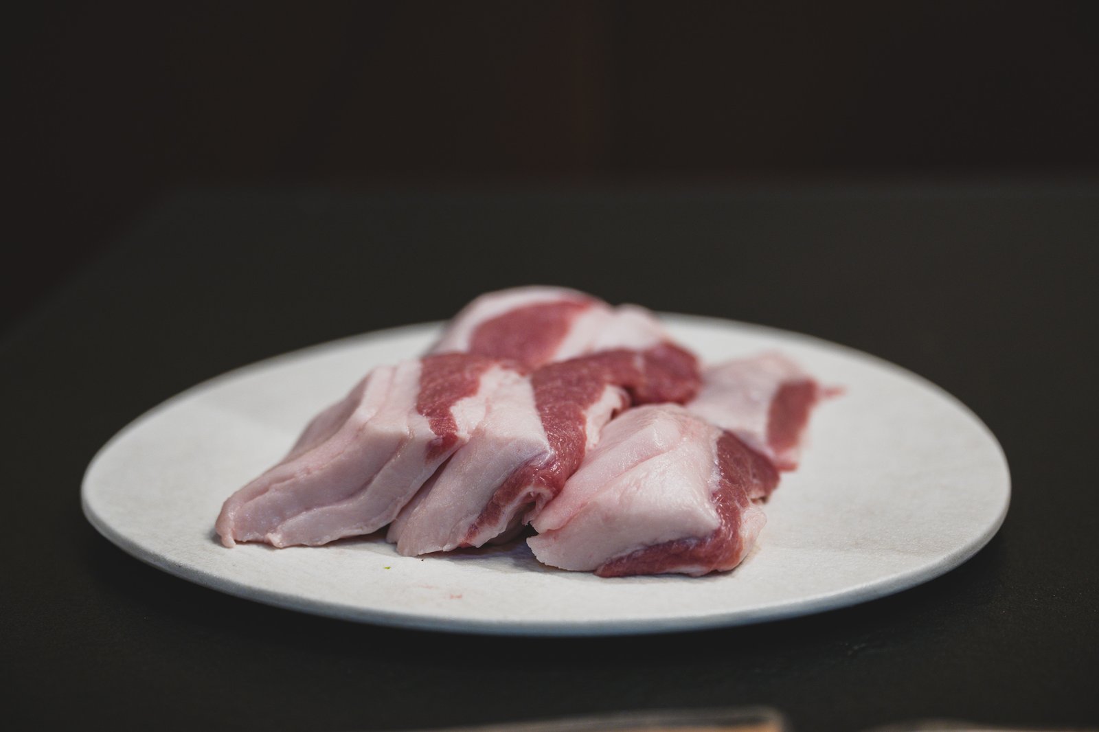 Raw, thick-cut pork jowl on a plate before grilling
