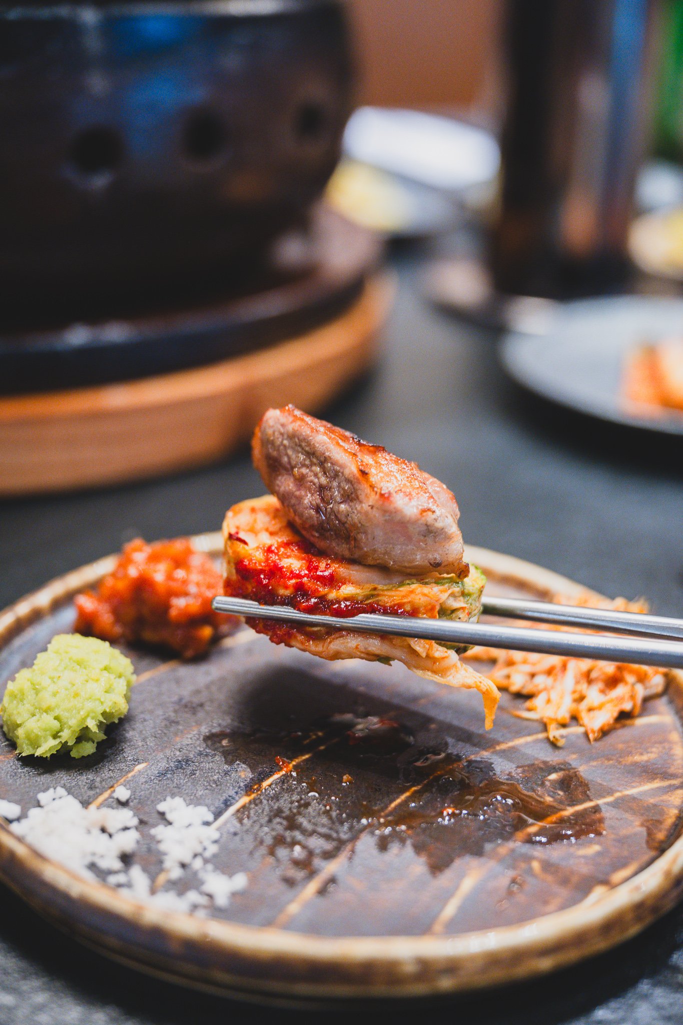 A piece of grilled pork being wrapped in kimchi with chopsticks