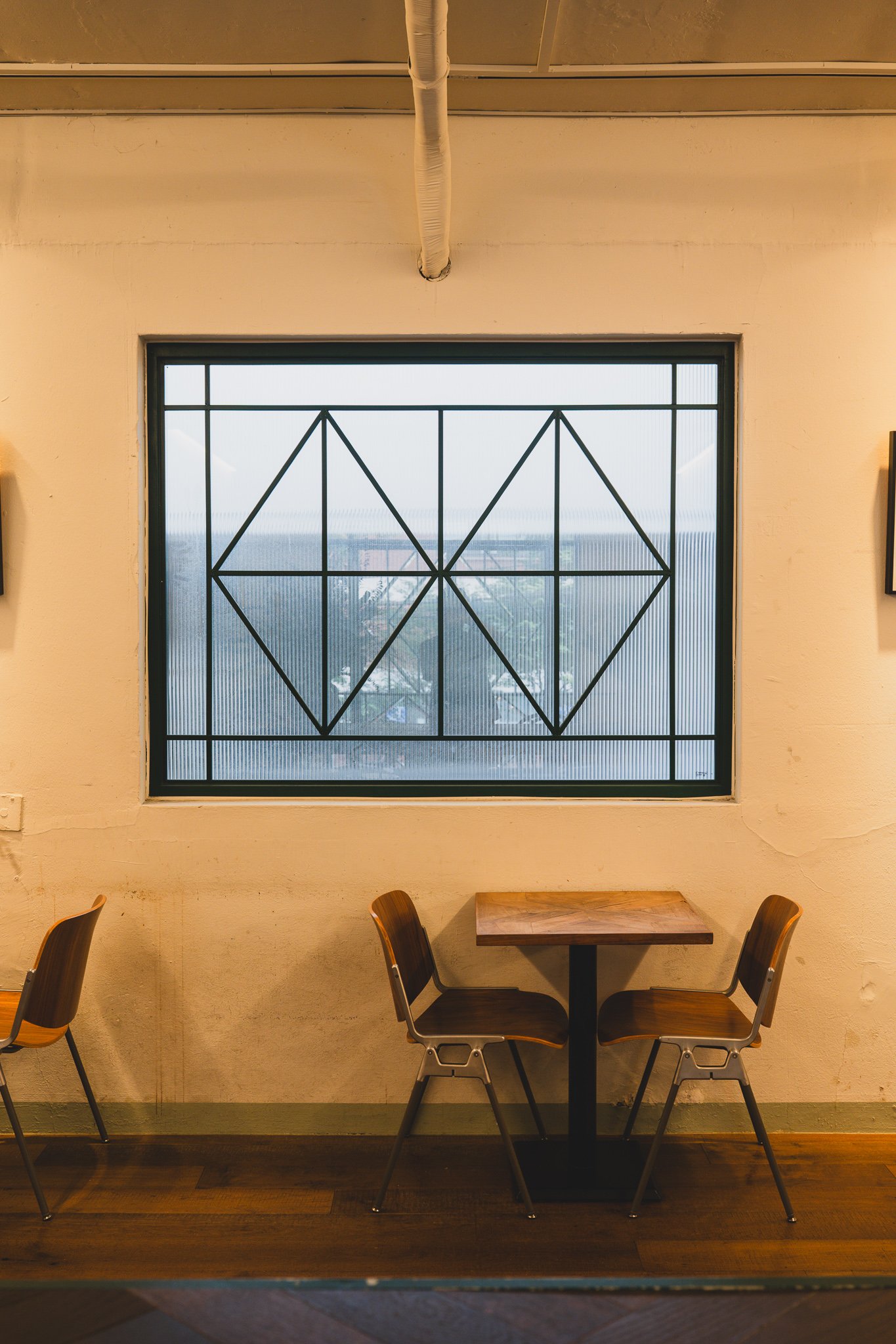 A two-seater table beside a window with a geometric diamond-pattern frame
