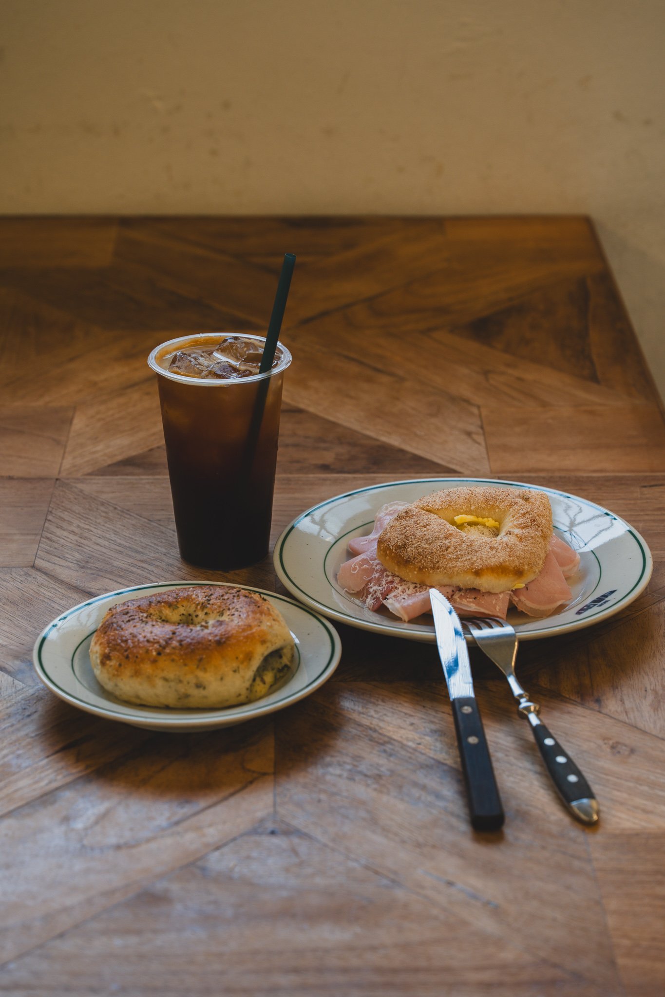 A basil bagel, cotto sandwich, and iced americano arranged on a table