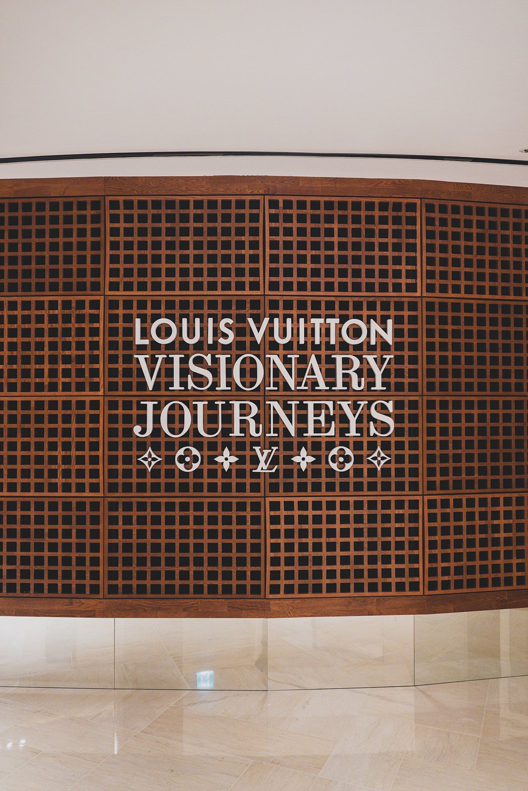 Entrance wall reading "Louis Vuitton Visionary Journeys" in a curved wood-lattice display