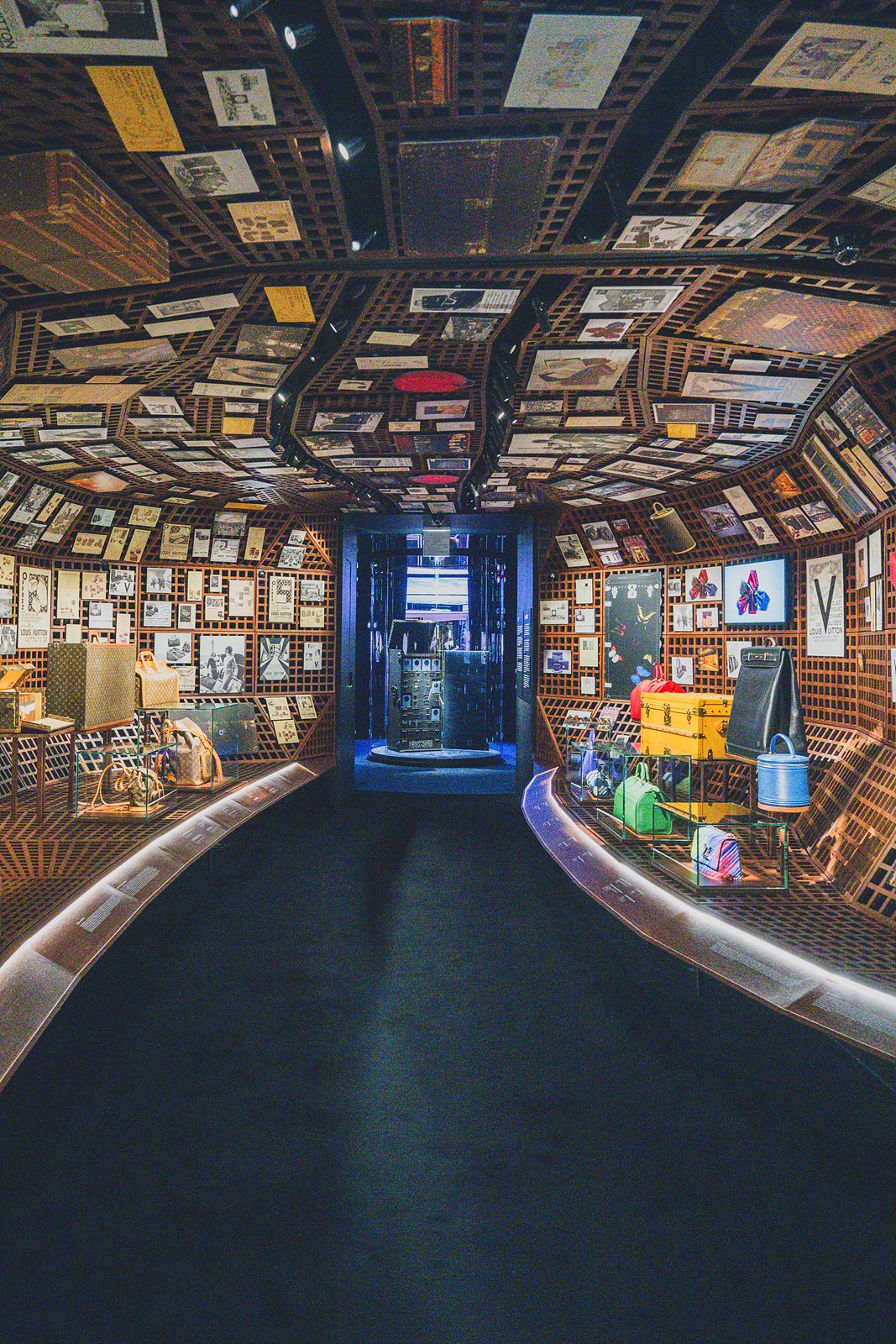 A second angle of the same curved archive room, continuing past a lit display case of colorful bags
