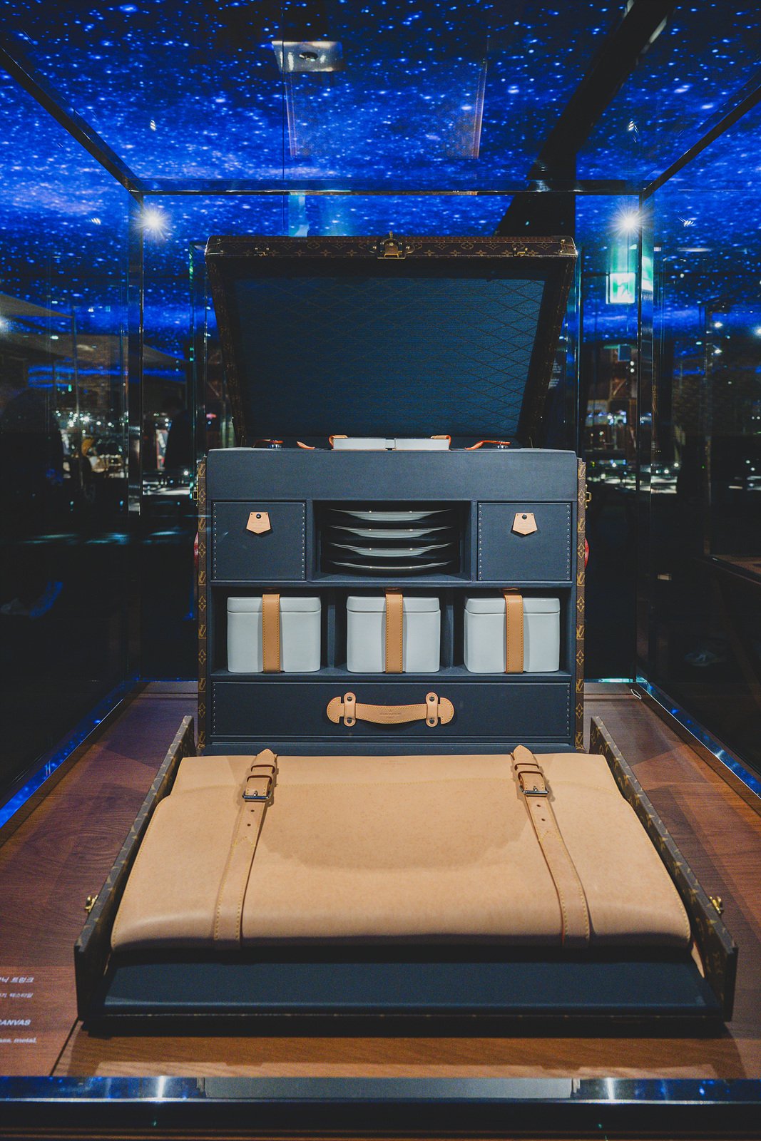 A fully unpacked Louis Vuitton picnic trunk, canisters and a serving tray arranged under a starry ceiling display