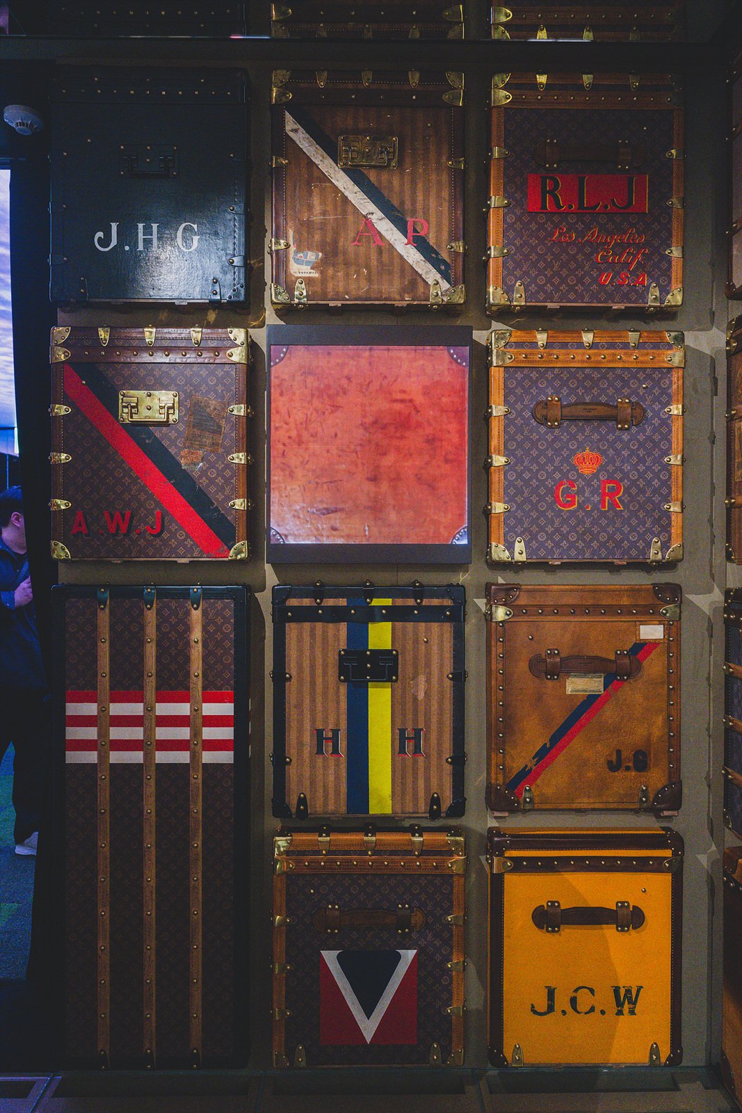 A wall of vintage-style trunks, each customized with a different owner's painted initials and stripes
