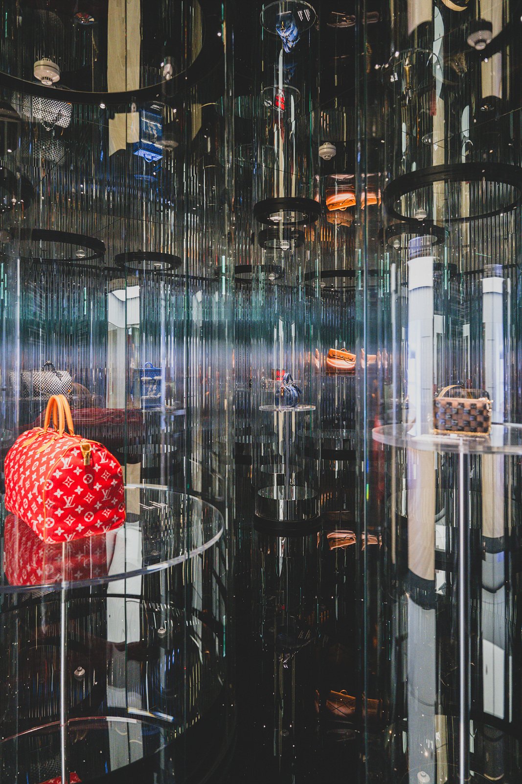 Mirrored display room reflecting Louis Vuitton bags, including a red monogram Keepall, into infinity