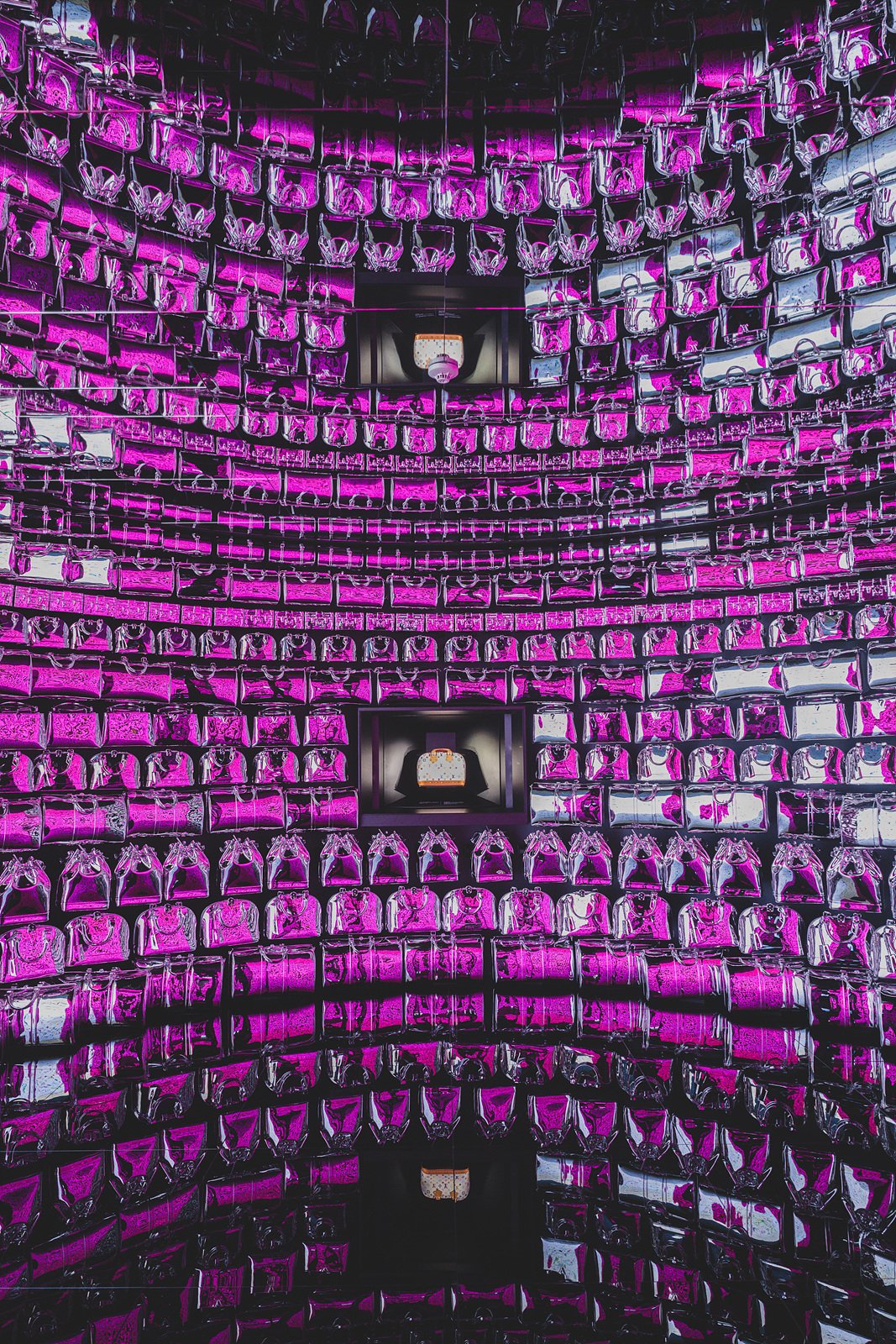 A kaleidoscope-mirrored room reflecting a Louis Vuitton bag display in vivid magenta