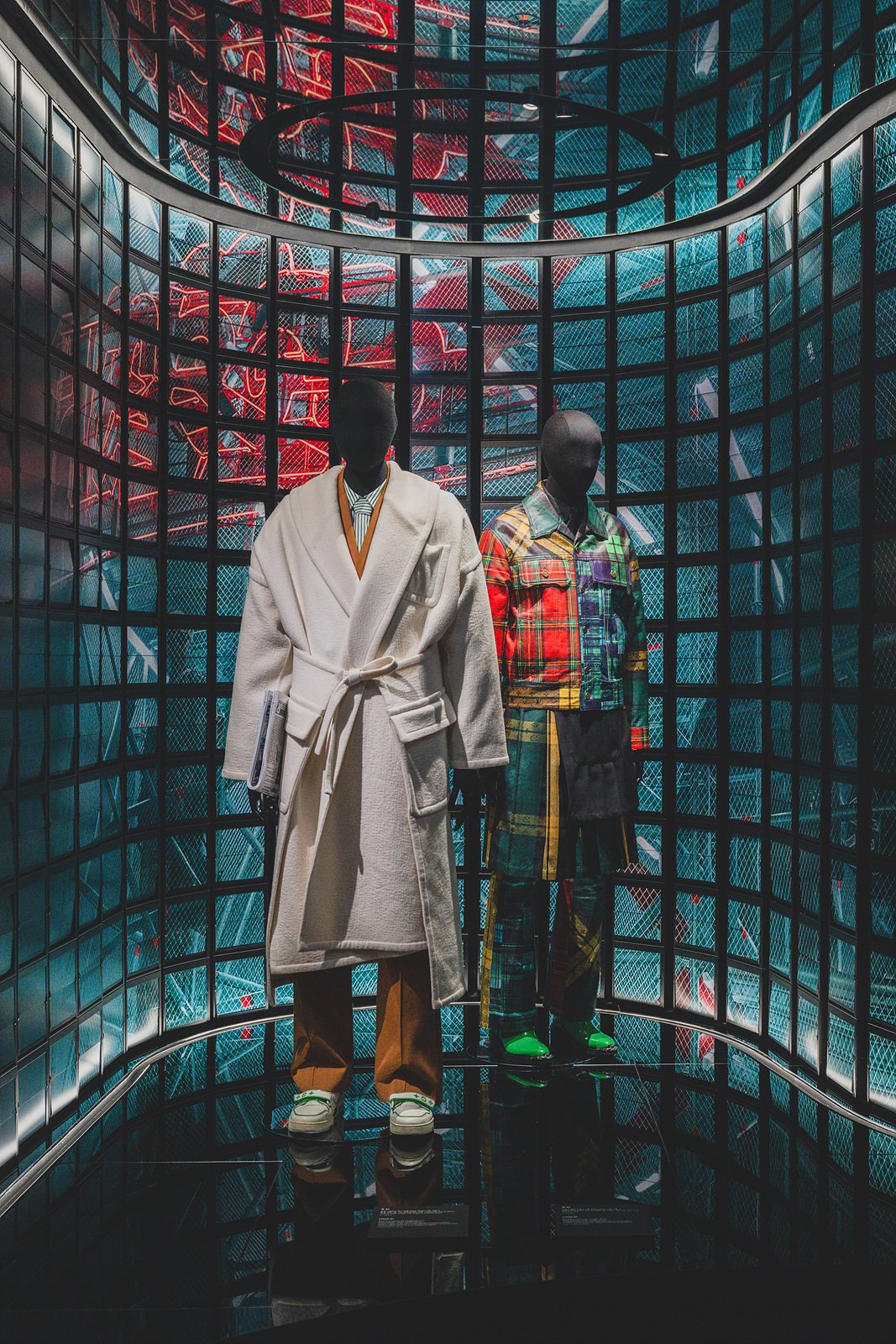 Two mannequins in a mirrored room wearing Louis Vuitton runway looks, lit in blue and red