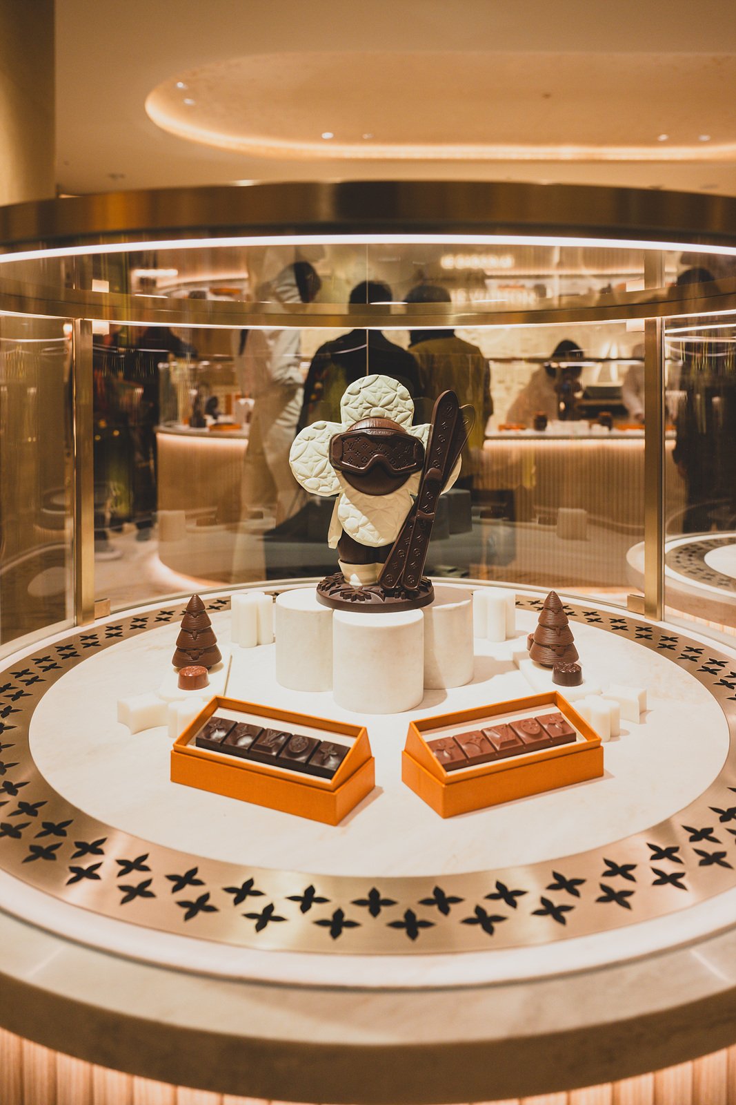 A display case with a chocolate figure dressed for skiing, goggles and skis included, next to boxes of monogram chocolates
