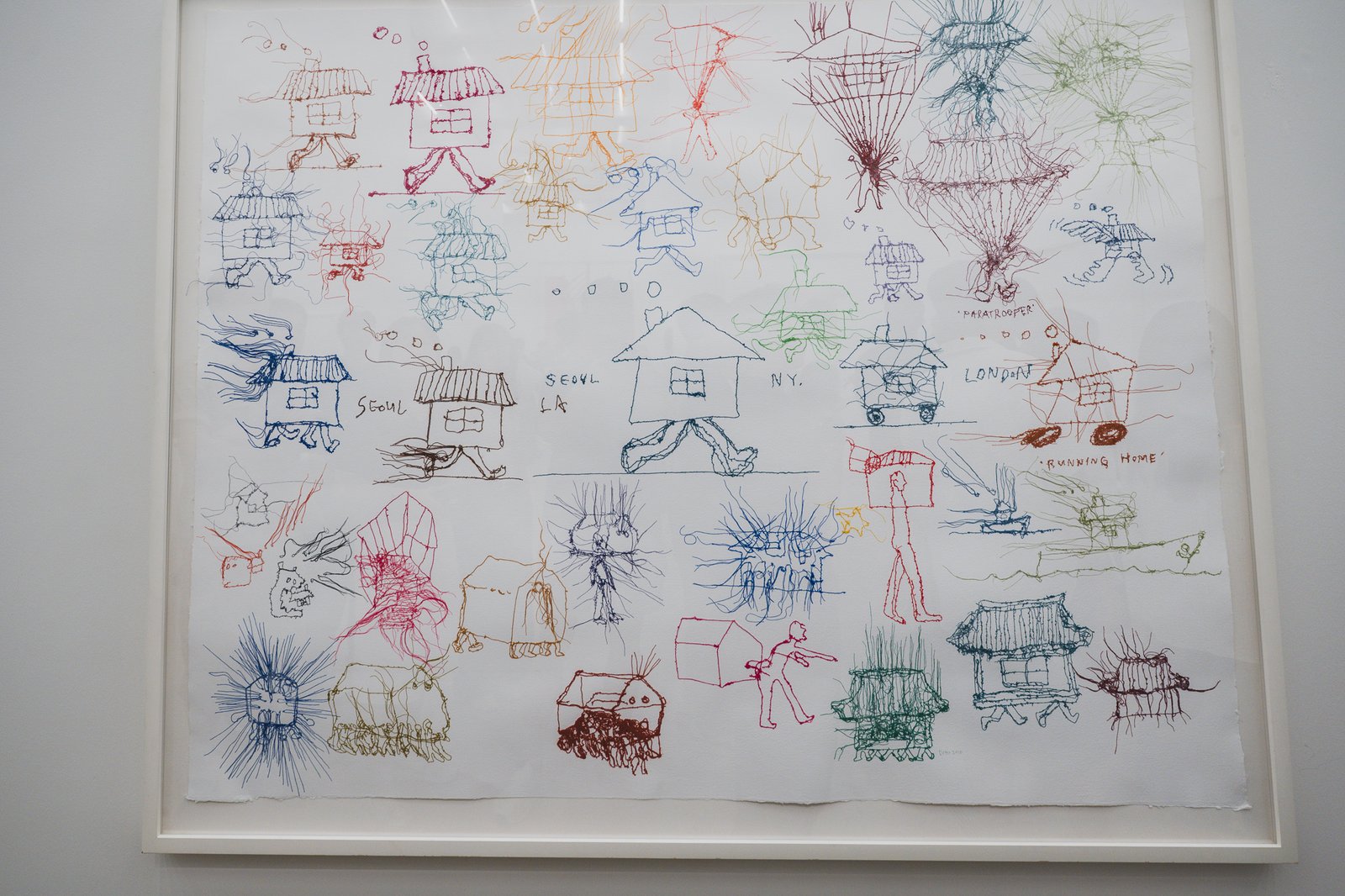 Embroidered thread drawing of houses with human legs walking between Seoul, LA, New York, and London