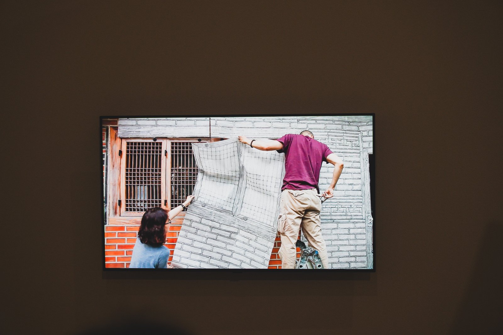 Video installation showing two people making a large frottage rubbing on an actual hanok exterior wall