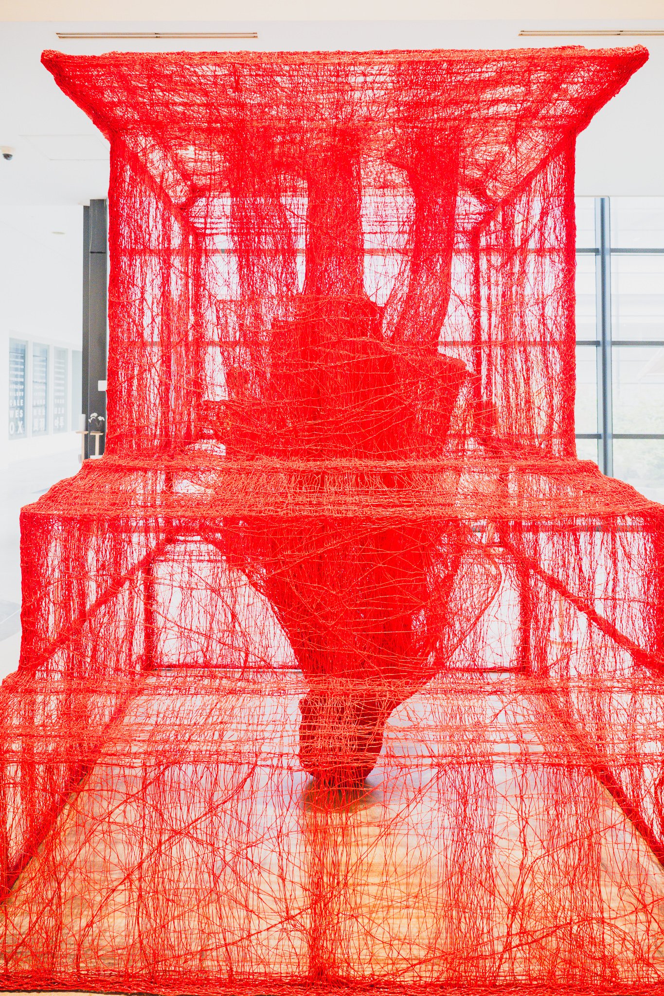 Large red thread hanok roof structure with a human silhouette visible through the fabric from inside