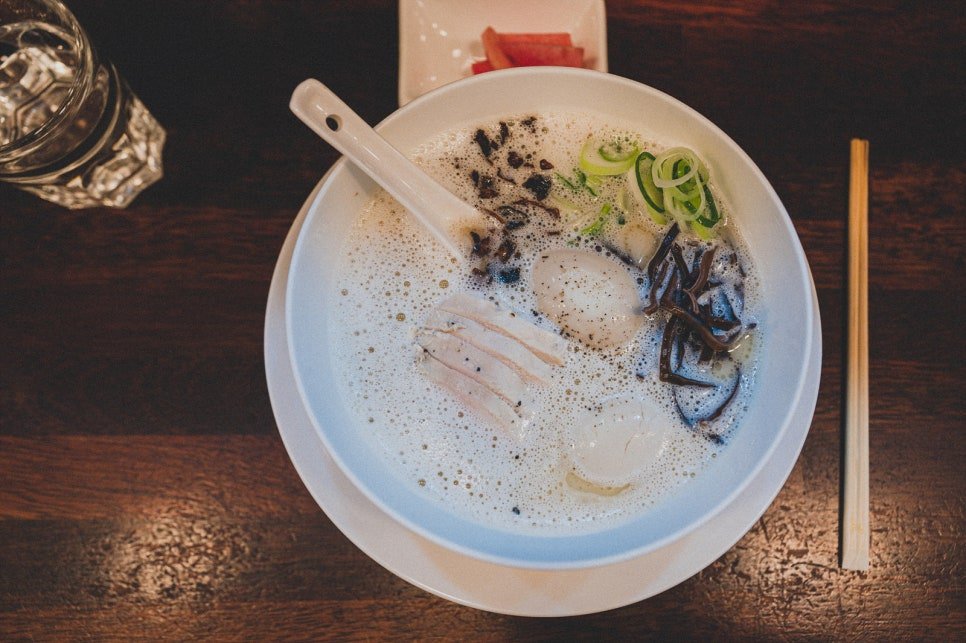 Overhead view of a bowl of pai-tan ramen with sliced pork, a soft-boiled egg, black fungus, and scallions in a creamy white broth