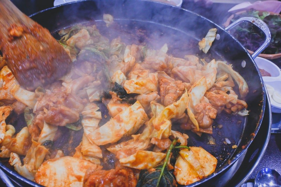 Overhead view of raw marinated chicken and vegetables in a large cooking pan, mid-stir-fry with visible steam