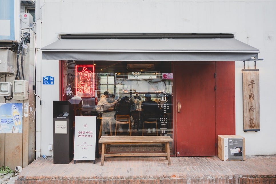 Storefront of Jinjung Woo Yuk Myeon Gwan, a wooden sign reading "牛肉面館" hanging beside a red door, with a placard noting four consecutive years on the Michelin Guide