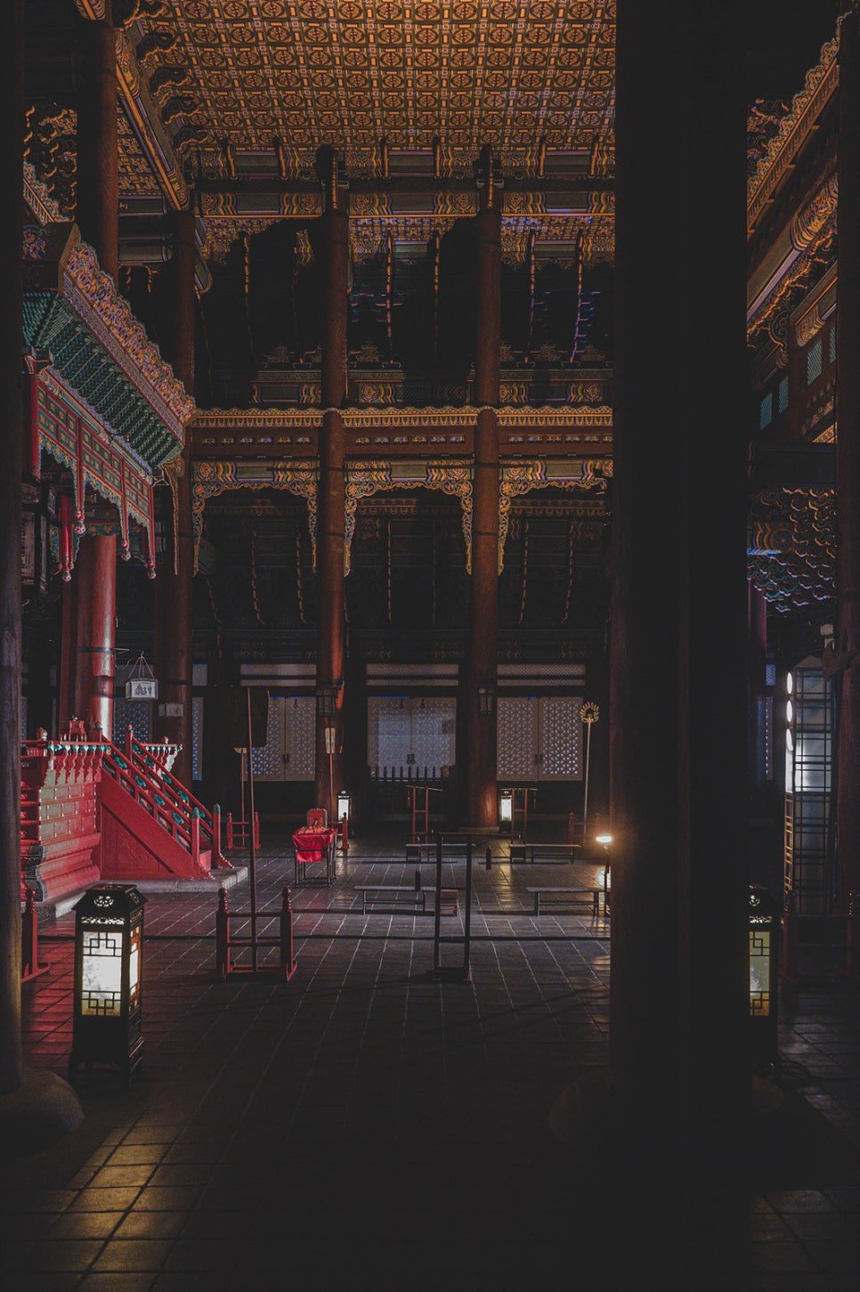 Ornate painted ceiling and eaves inside Geunjeongjeon's covered walkway, lit at night