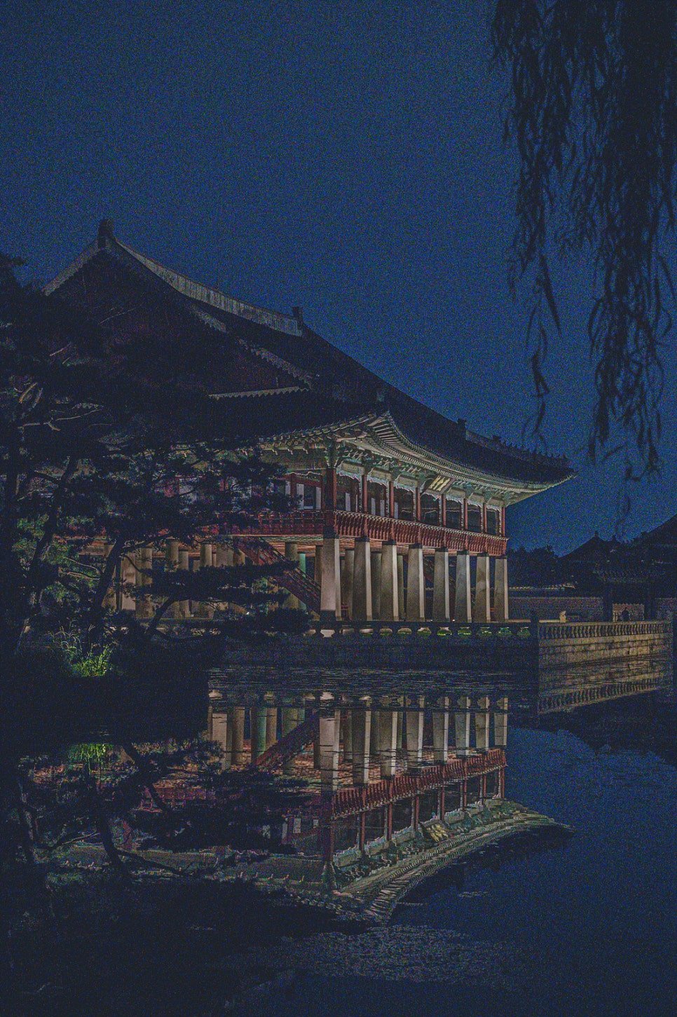 A diagonal view of Gyeonghoeru through overhanging willow branches, reflected in the pond
