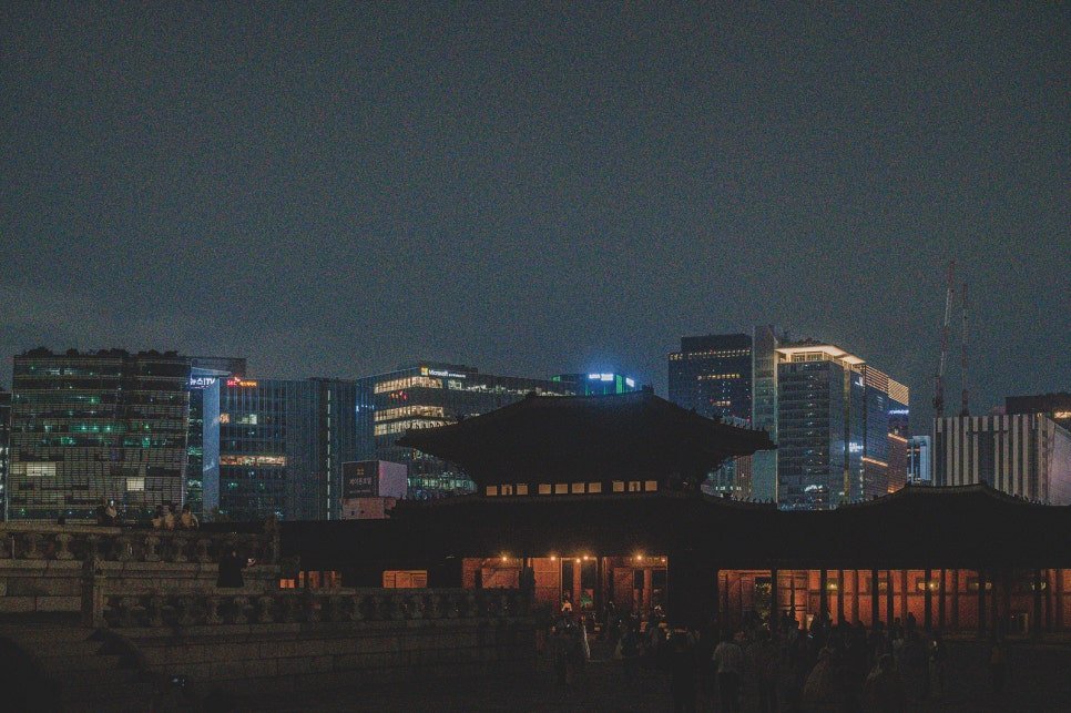 Gyeongbokgung's traditional rooftops silhouetted against Seoul's modern skyline of illuminated office towers