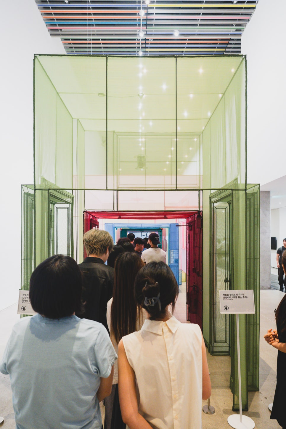 Visitors walking through Do Ho Suh's translucent fabric door-frame installation, each doorway a different color