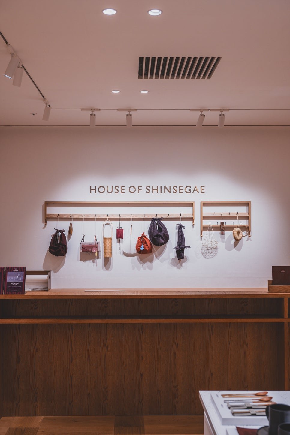 Storefront wall reading "HOUSE OF SHINSEGAE" with a row of handmade bags and pouches hanging from wooden pegs