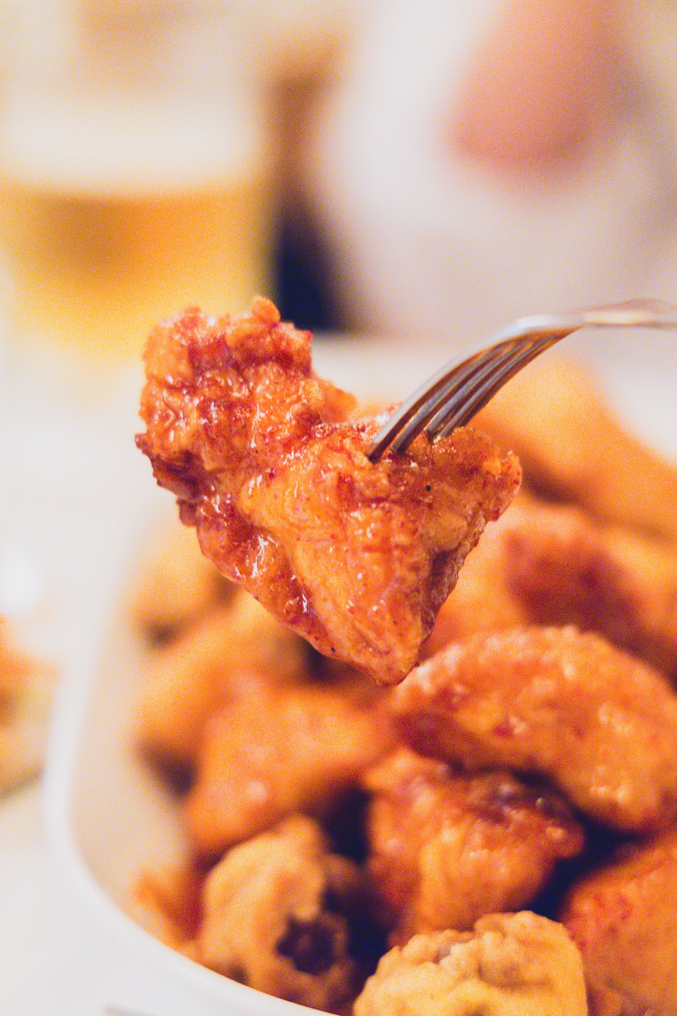 Close-up of a piece of seasoned (yangnyeom) chicken held with a fork