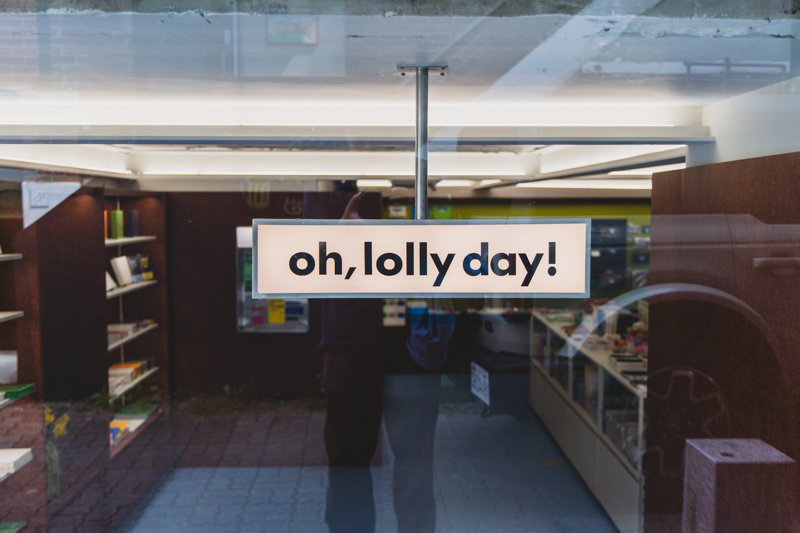 The "oh, lolly day!" lightbox sign hanging inside the store, warmly lit in yellow