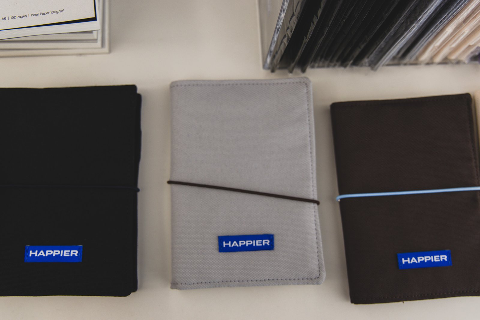 Three finished cover samples in black, gray, and brown, each with a blue "HAPPIER" label