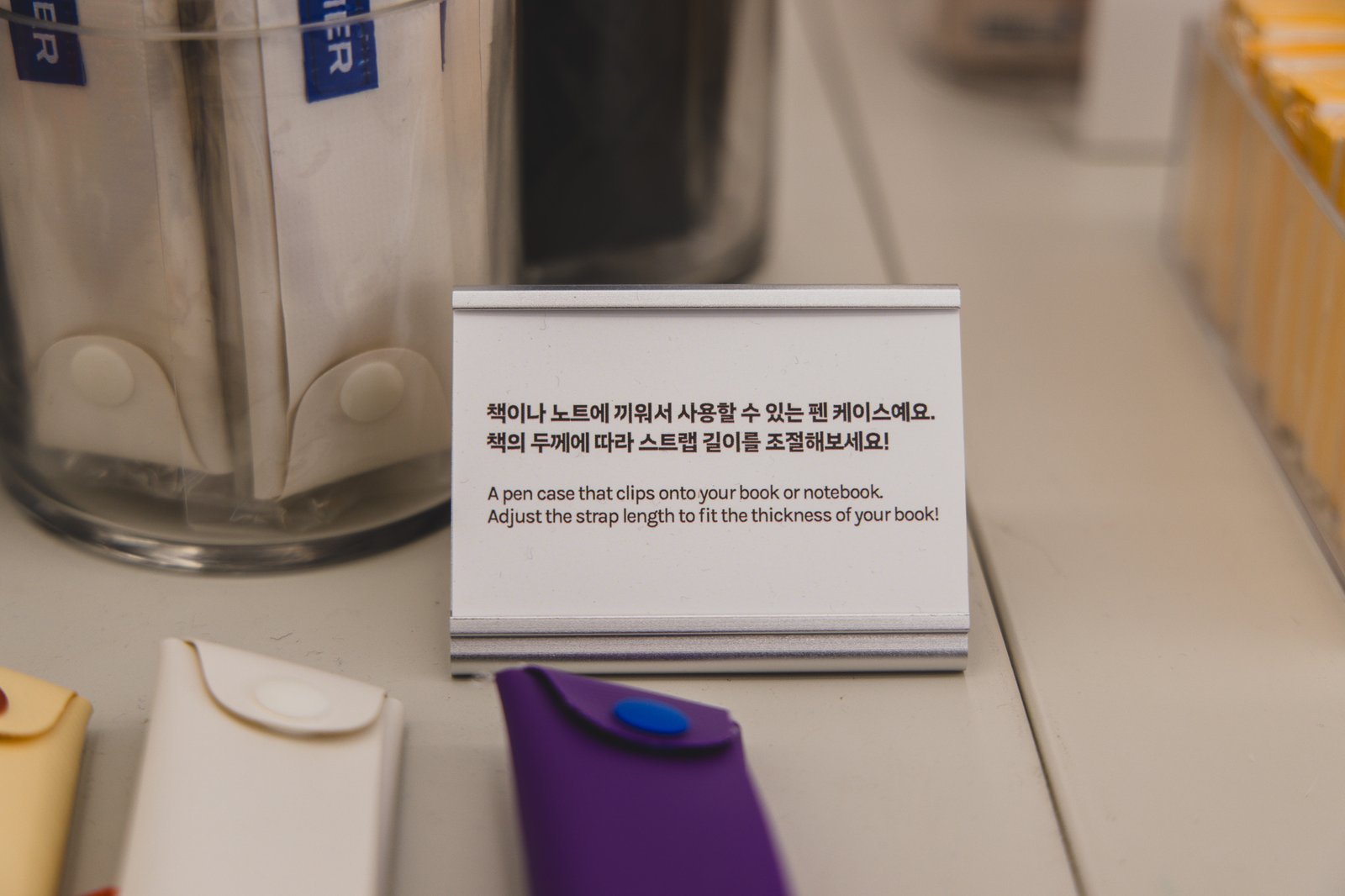 A sign explaining the pen case: it clips onto a book or notebook, with an adjustable strap for different book thicknesses