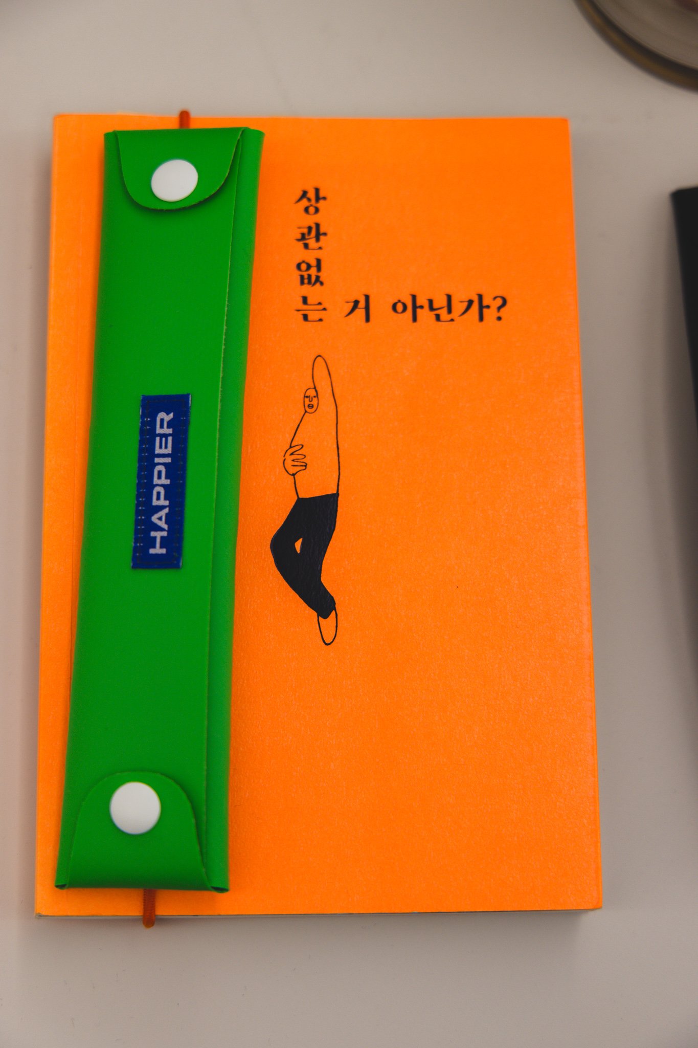 The finished setup: an orange illustrated notebook with a green TPL string pen case attached vertically