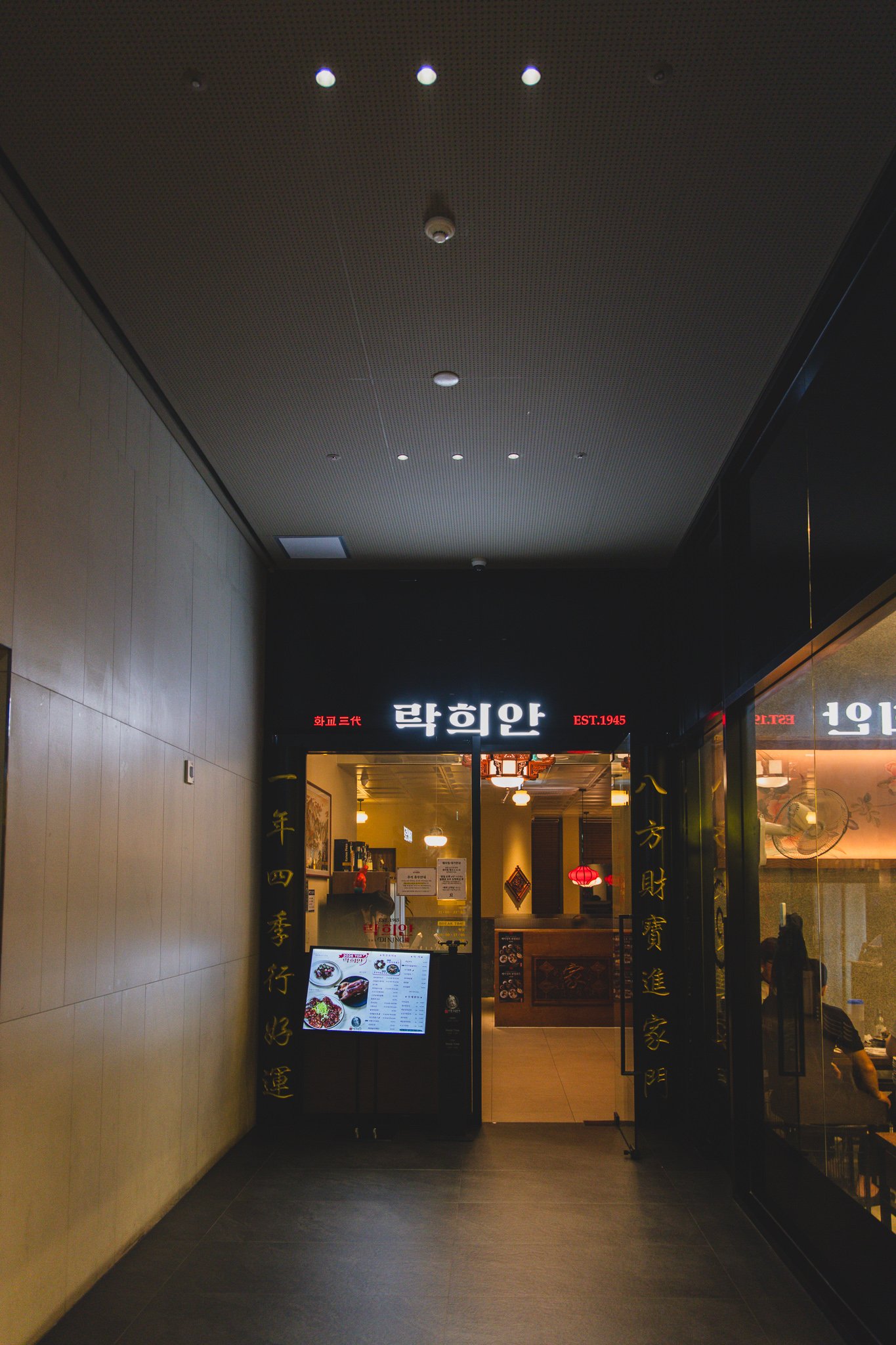 Rakhian's neon signage at the end of a corridor reading "화교三代" (third-generation hwagyo) and "EST.1945" in red and white lettering above the entrance
